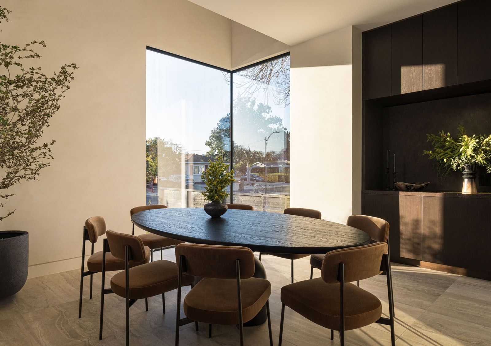 This light-filled dining room combines soaring corner glazing, warm timber cabinetry, and a round dining table to create an elegant space for everyday meals and entertaining.