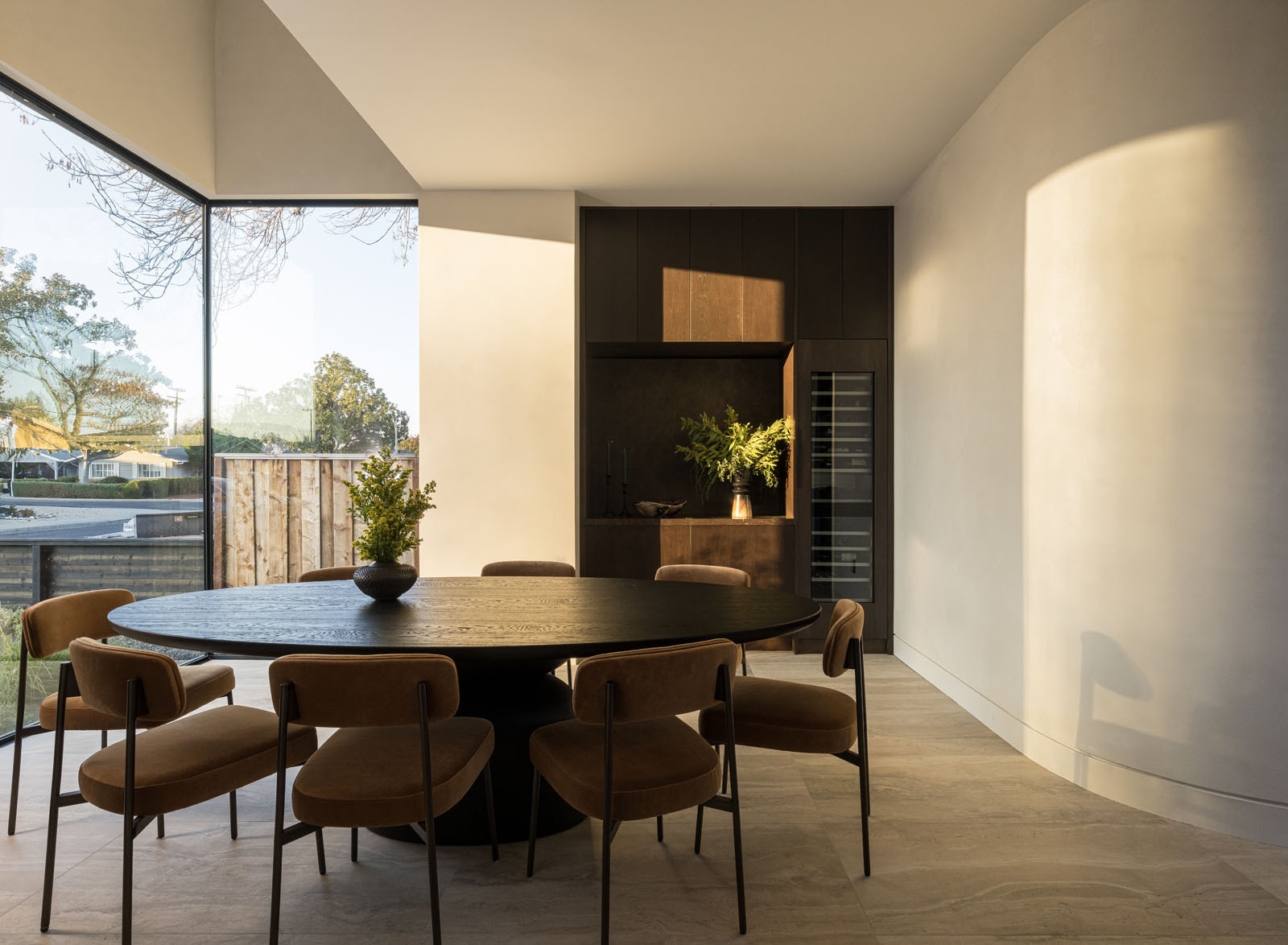 This light-filled dining room combines soaring corner glazing, warm timber cabinetry, and a round dining table to create an elegant space for everyday meals and entertaining.