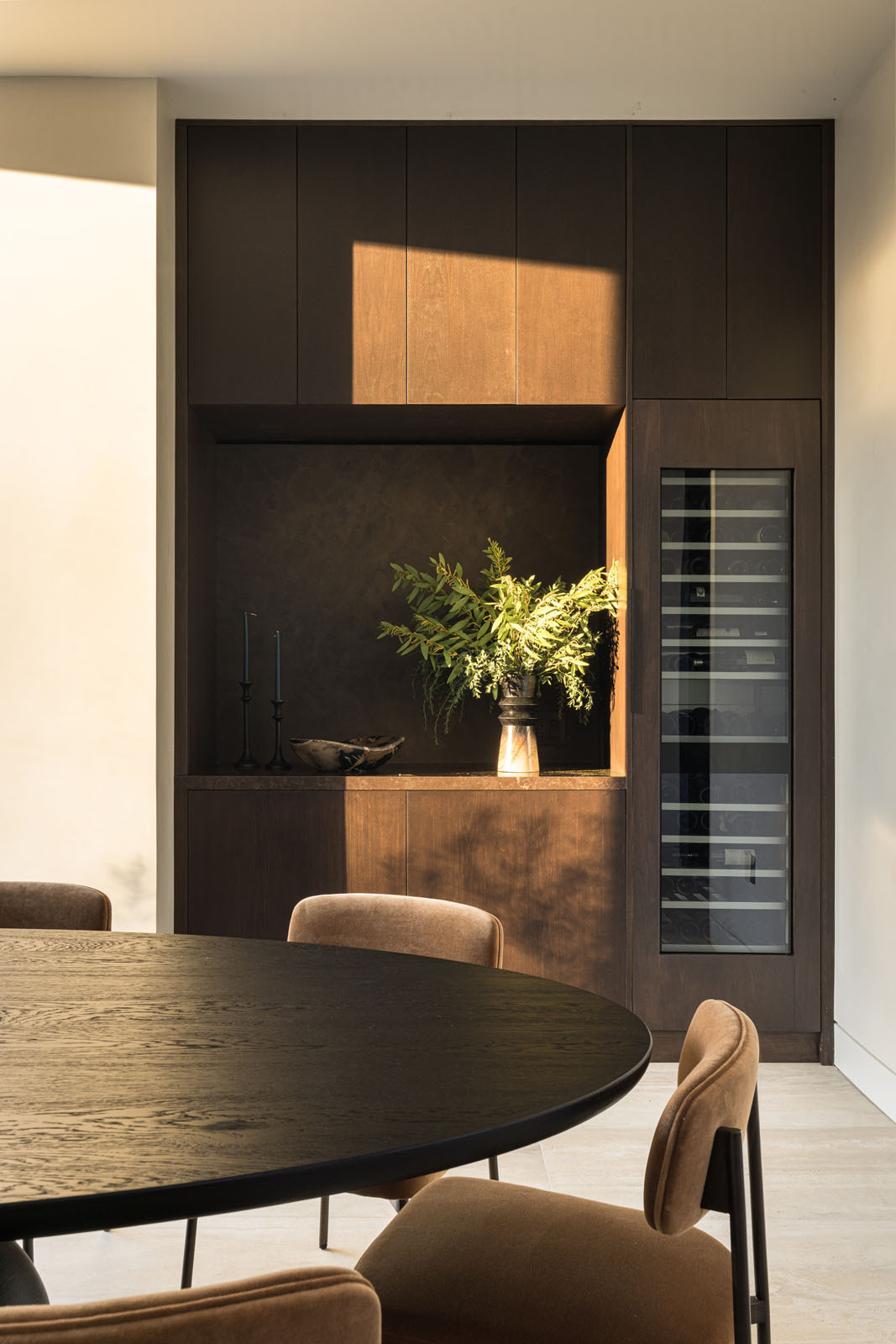 This light-filled dining room combines soaring corner glazing, warm timber cabinetry, and a round dining table to create an elegant space for everyday meals and entertaining.