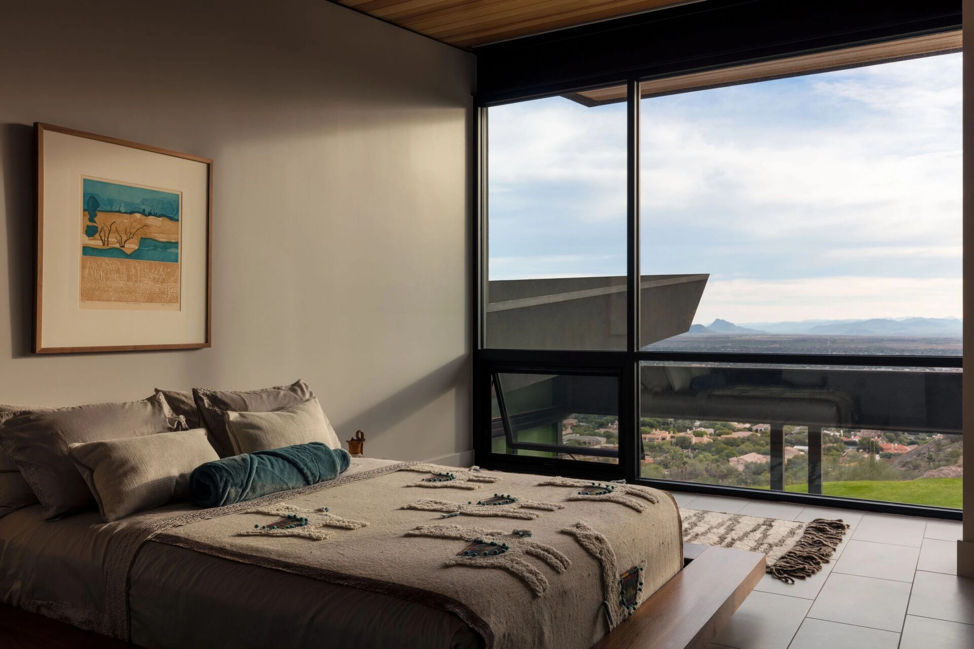 A guest bedroom features floor-to-ceiling windows that capture impressive views across the surrounding landscape.