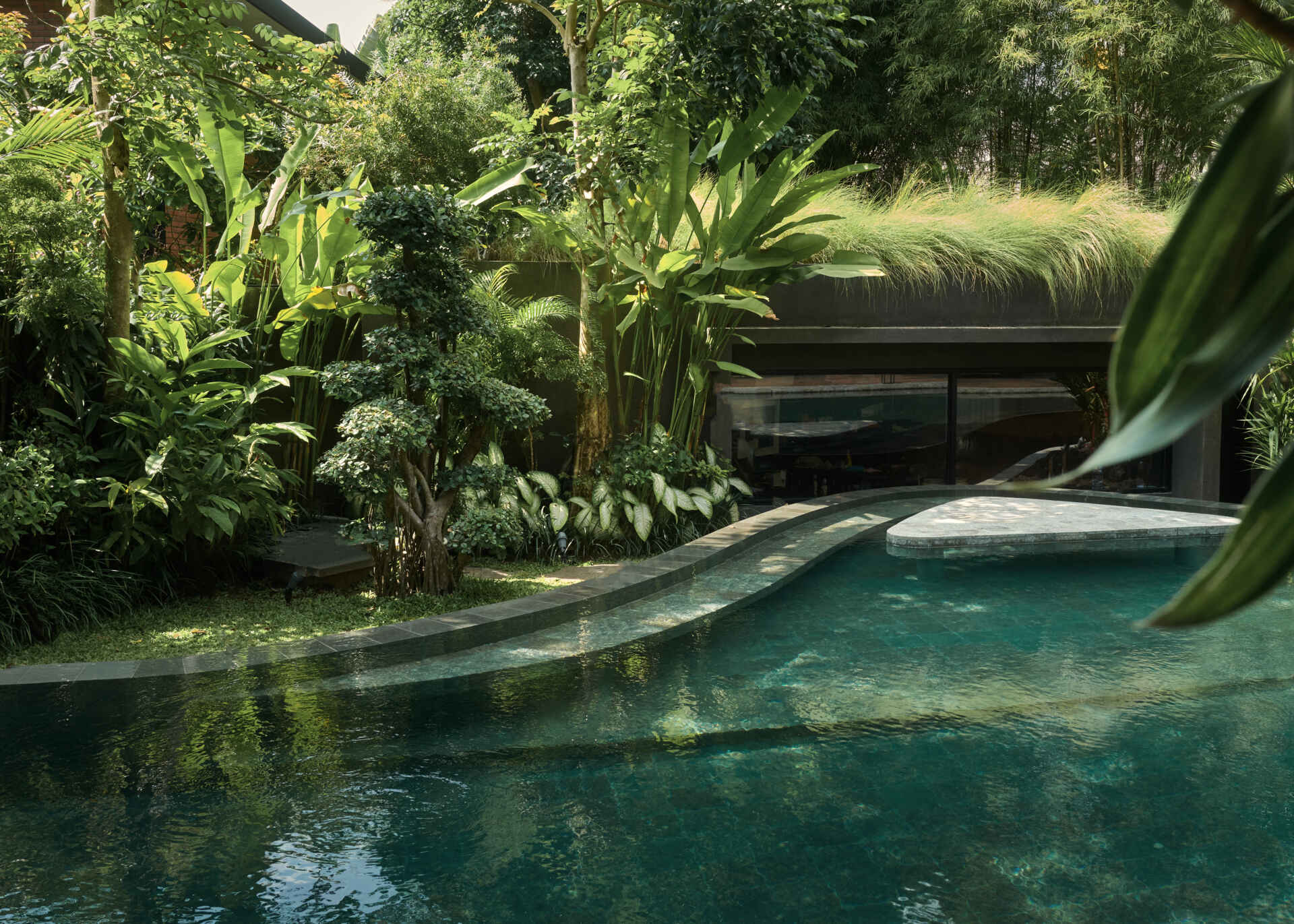 A second swimming pool with a curved edge, extends alongside this open ground-floor setting, reinforcing the connection between indoor and outdoor living. Positioned beside the social spaces, the water reflects changing light throughout the day while adding another layer of openness to the design.