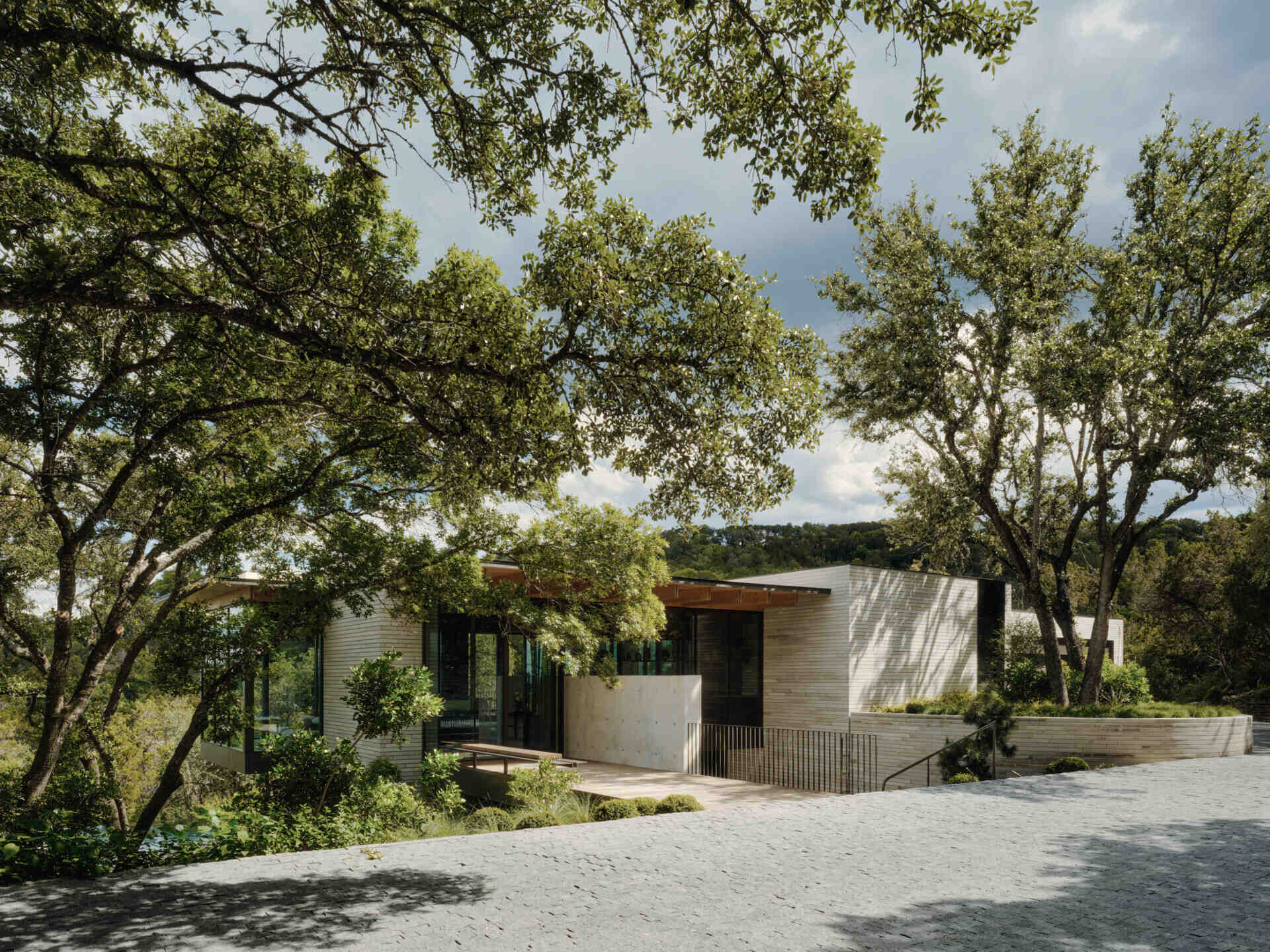 Native terraces and limestone create an inviting arrival sequence that blends architecture with the Texas hillside.