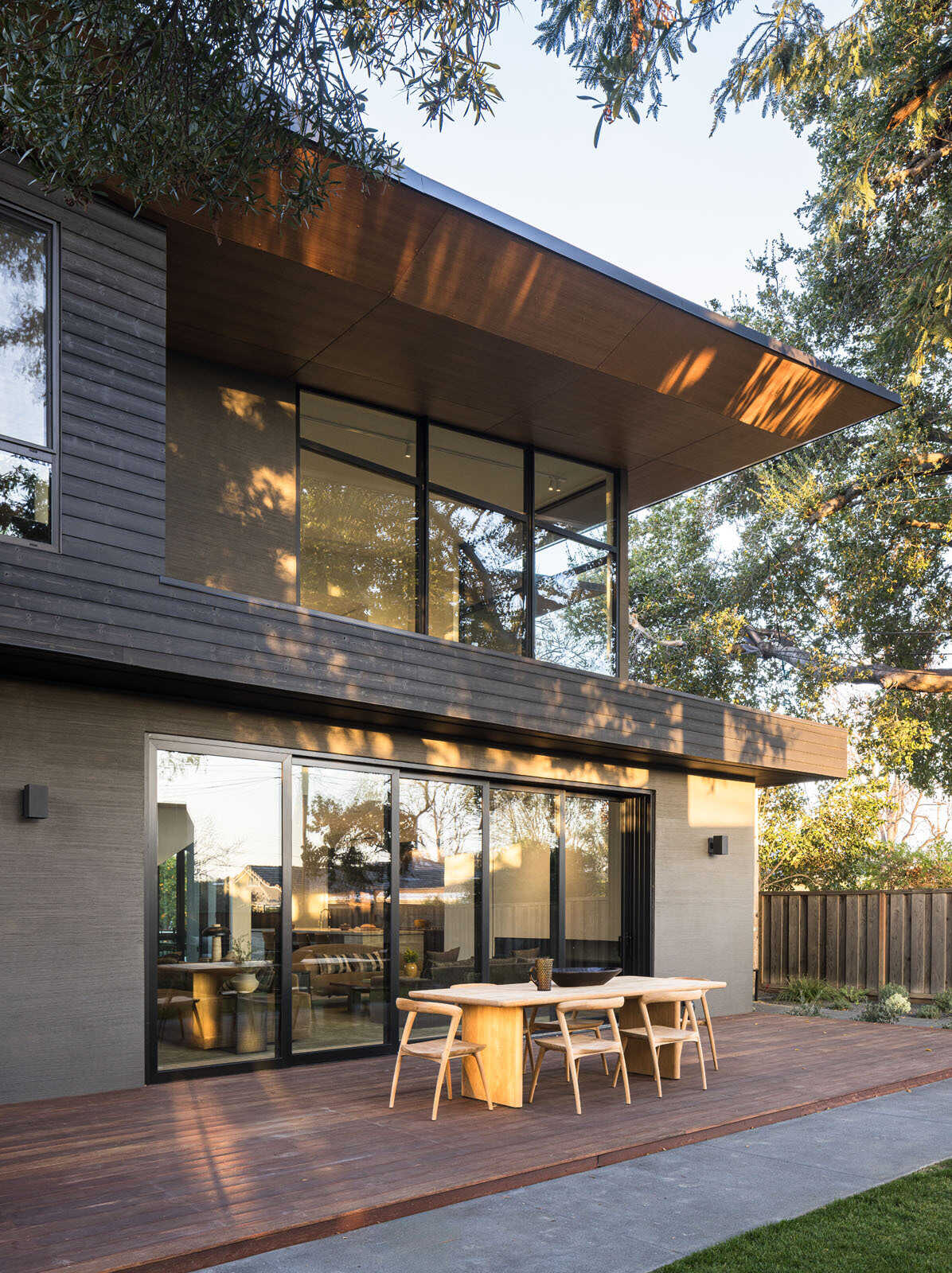 Step onto a warm timber deck where oversized sliding doors, shaded outdoor dining, and views of mature trees create the perfect extension of this Silicon Valley home.