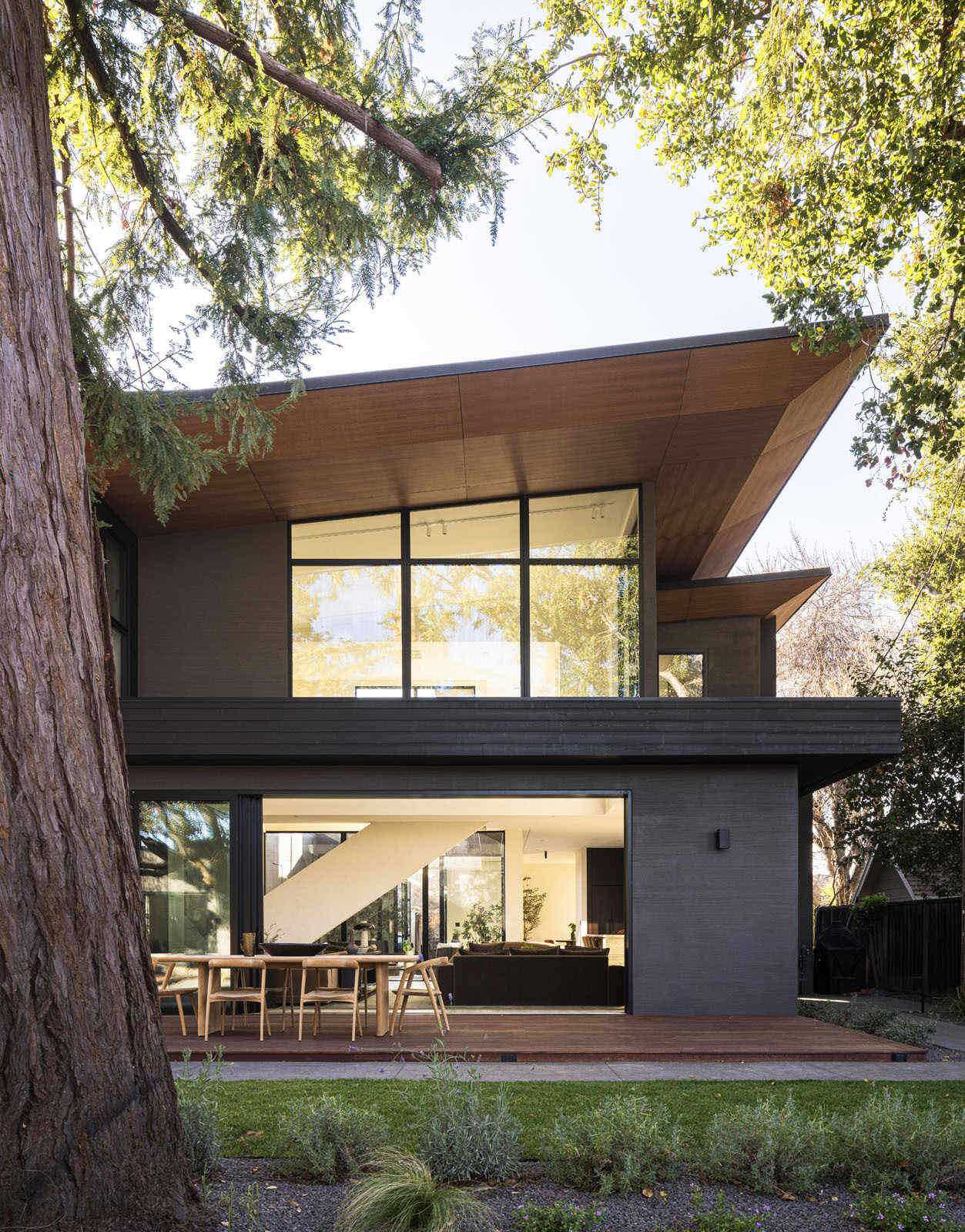 Step onto a warm timber deck where oversized sliding doors, shaded outdoor dining, and views of mature trees create the perfect extension of this Silicon Valley home.