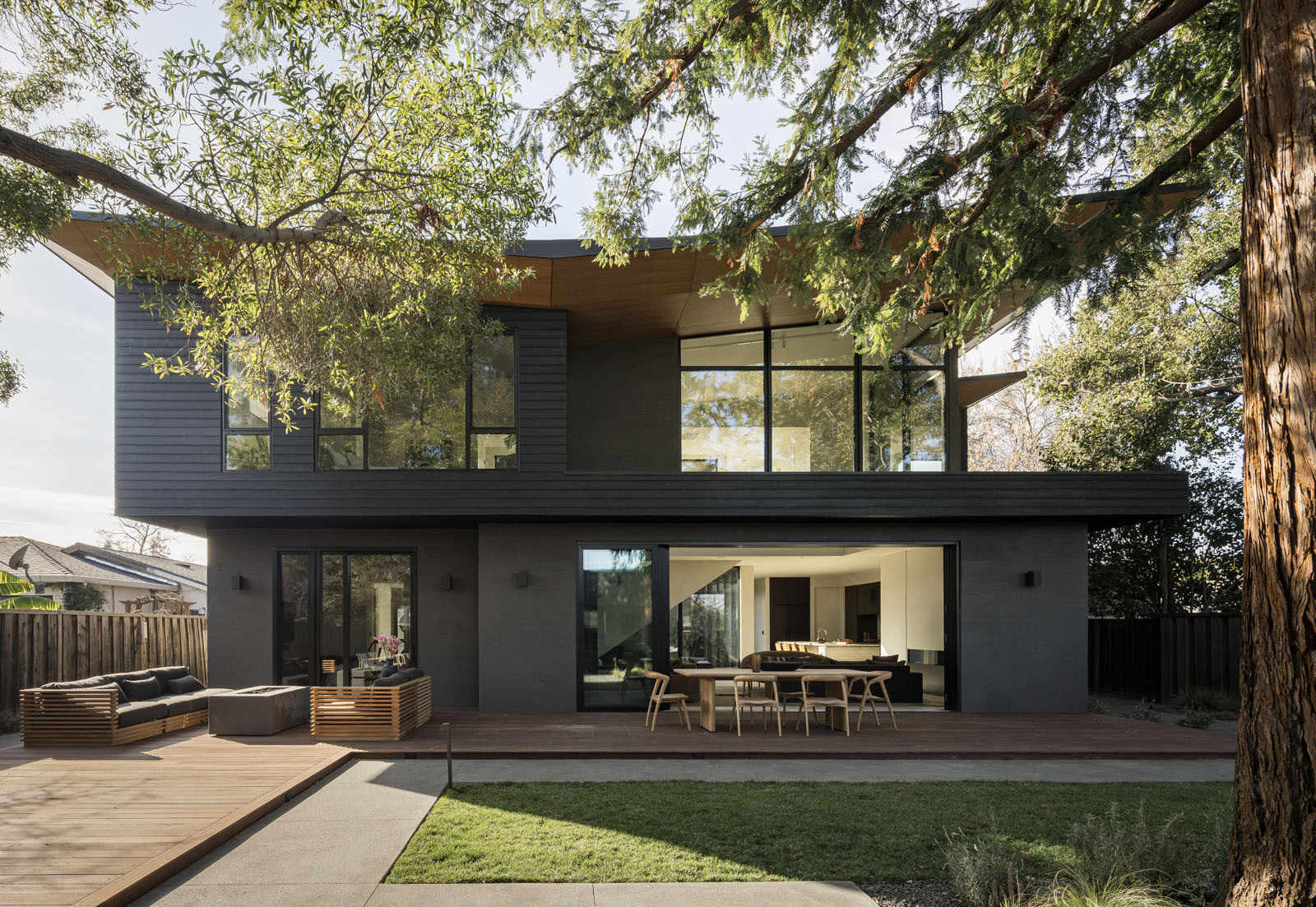 Step onto a warm timber deck where oversized sliding doors, shaded outdoor dining, and views of mature trees create the perfect extension of this Silicon Valley home.