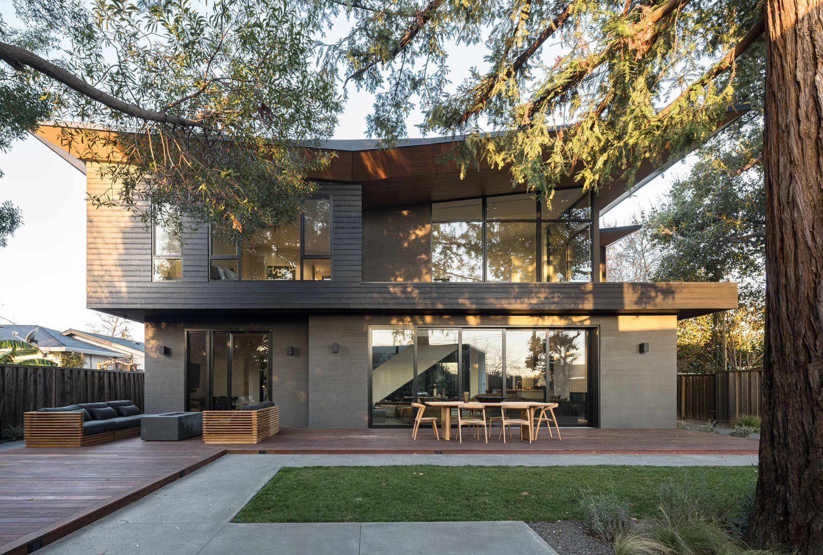 Step onto a warm timber deck where oversized sliding doors, shaded outdoor dining, and views of mature trees create the perfect extension of this Silicon Valley home.