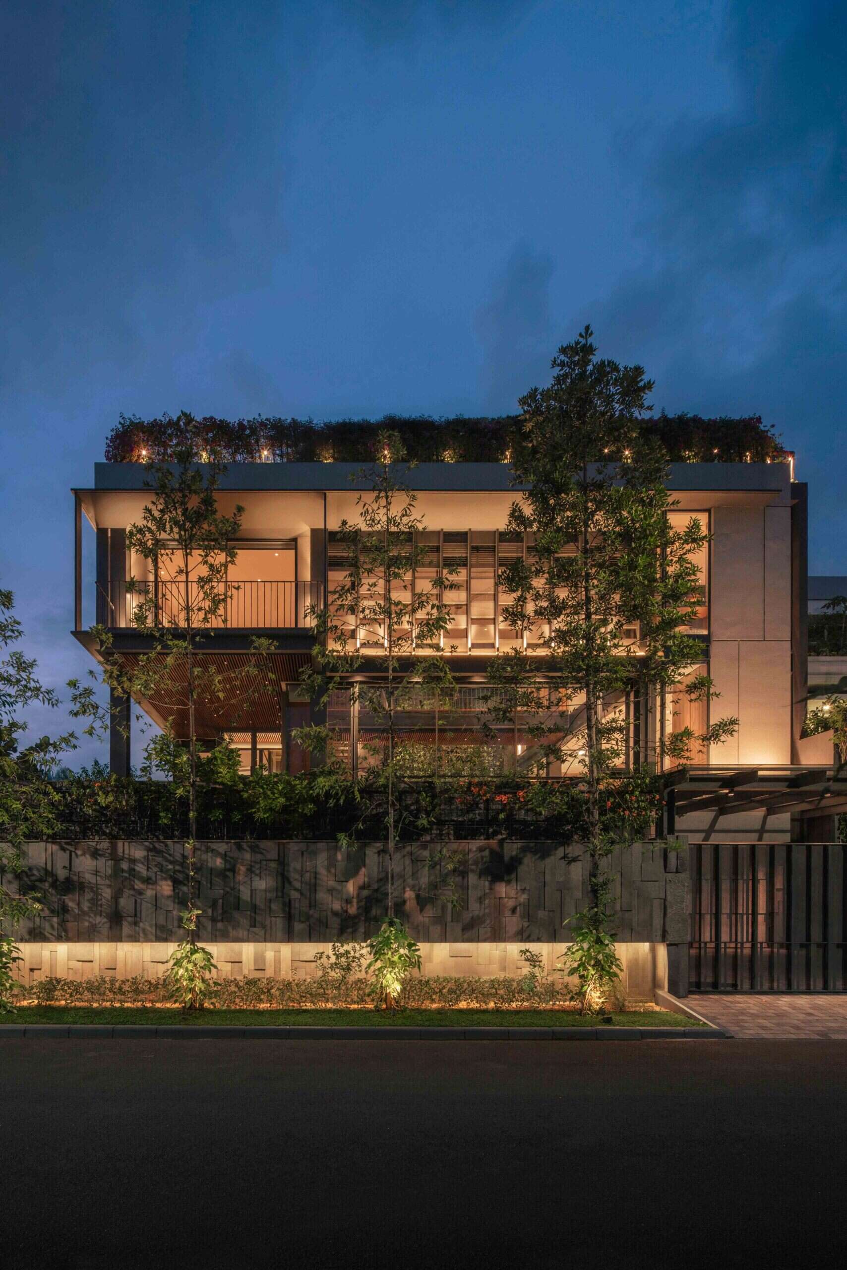Warm exterior lighting highlights the steel structure, textured walls and tropical planting throughout this contemporary Jakarta home.