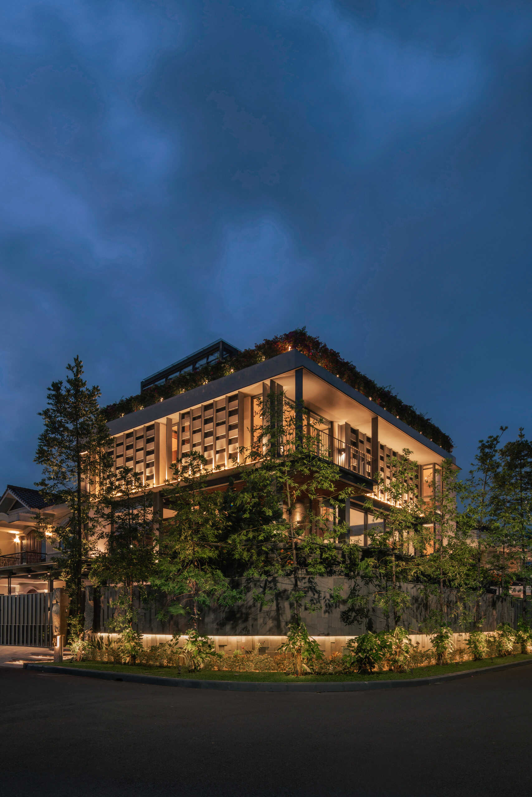 Warm exterior lighting highlights the steel structure, textured walls and tropical planting throughout this contemporary Jakarta home.