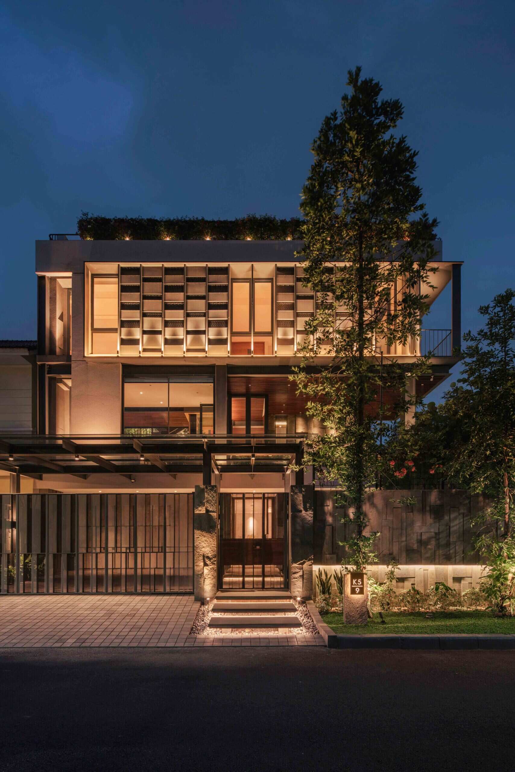 Warm exterior lighting highlights the steel structure, textured walls and tropical planting throughout this contemporary Jakarta home.