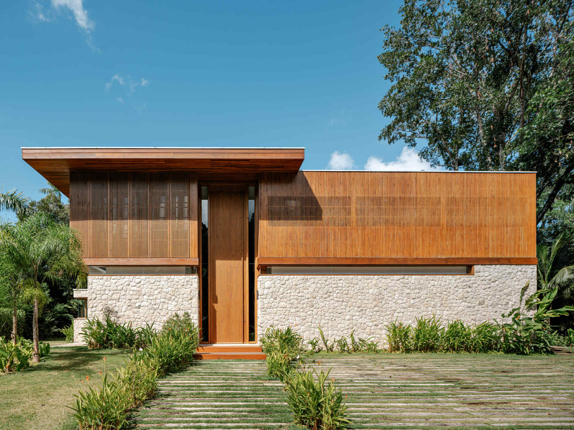From the street, concrete provides the structural framework, while moledo stone appears across sections of the facade, while slatted timber panels soften the appearance of the house while adding privacy.
Even the entrance hints at what lies beyond, with a double height wood front door that opens to reveal the living spaces and garden views.