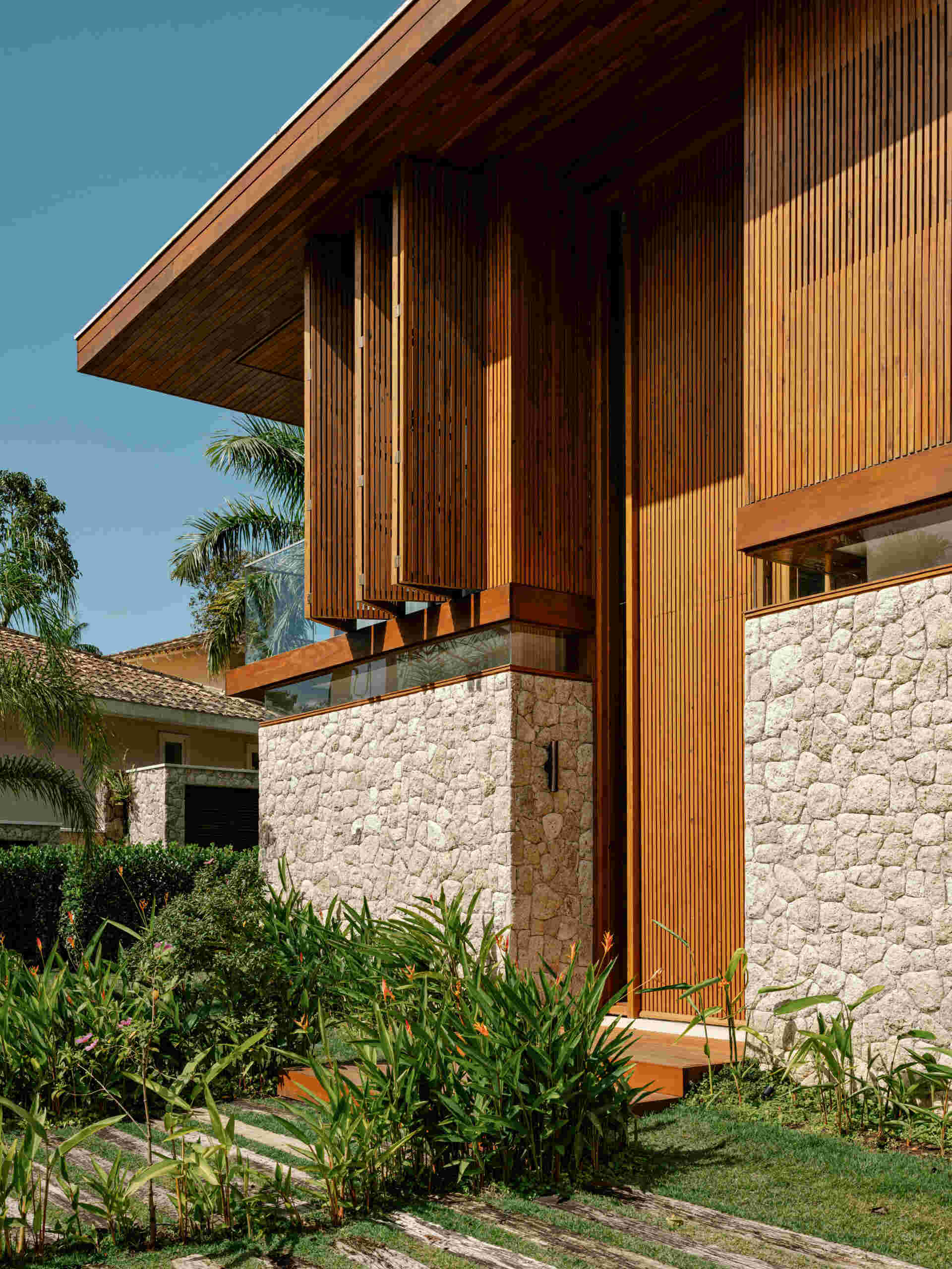 From the street, concrete provides the structural framework, while moledo stone appears across sections of the facade, while slatted timber panels soften the appearance of the house while adding privacy.
Even the entrance hints at what lies beyond, with a double height wood front door that opens to reveal the living spaces and garden views.