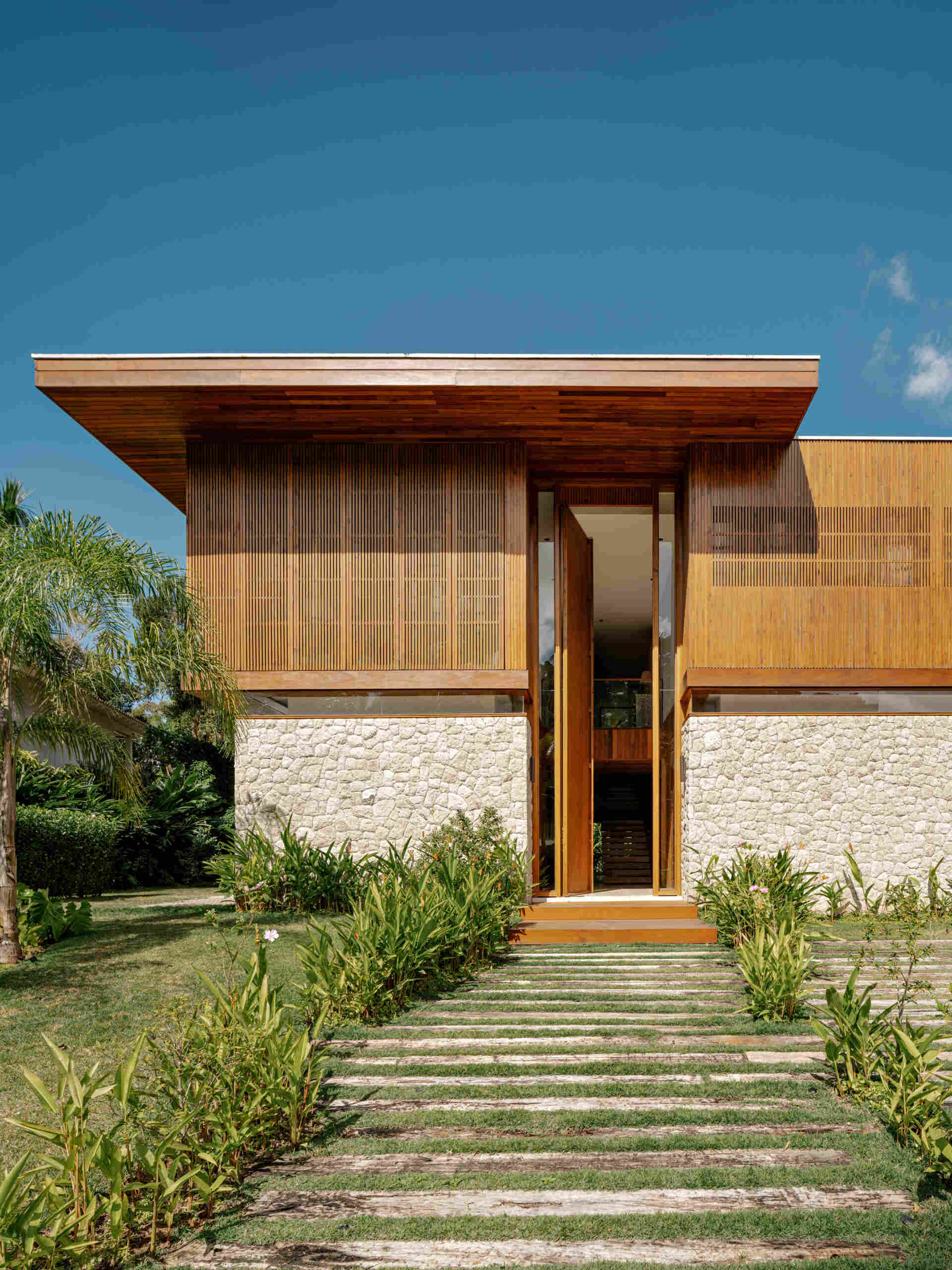 From the street, concrete provides the structural framework, while moledo stone appears across sections of the facade, while slatted timber panels soften the appearance of the house while adding privacy.
Even the entrance hints at what lies beyond, with a double height wood front door that opens to reveal the living spaces and garden views.