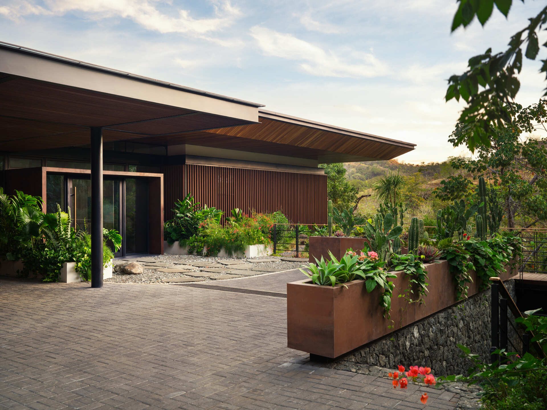 Stone pathways, warm timber, and tropical planting create an entrance that gradually introduces visitors to Casa Akíga.