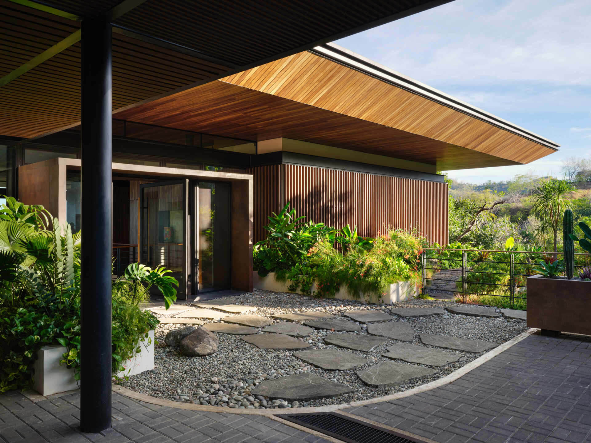 Stone pathways, warm timber, and tropical planting create an entrance that gradually introduces visitors to Casa Akíga.