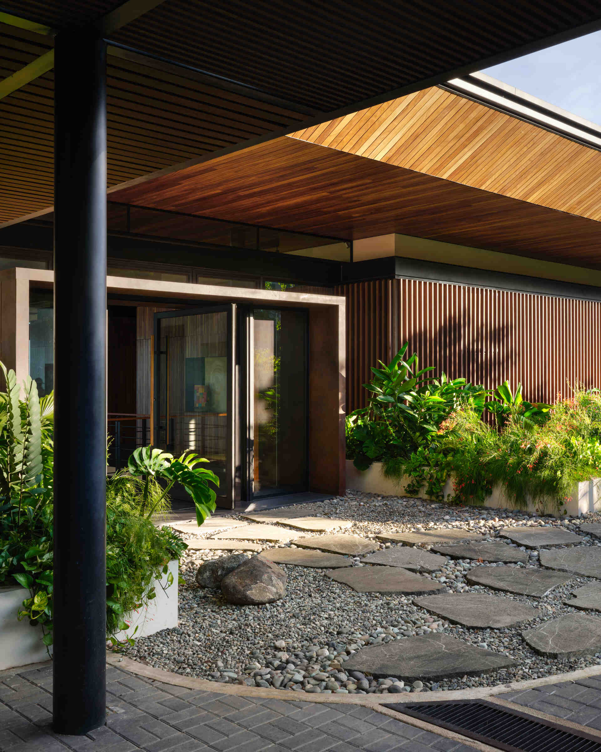 Stone pathways, warm timber, and tropical planting create an entrance that gradually introduces visitors to Casa Akíga.
