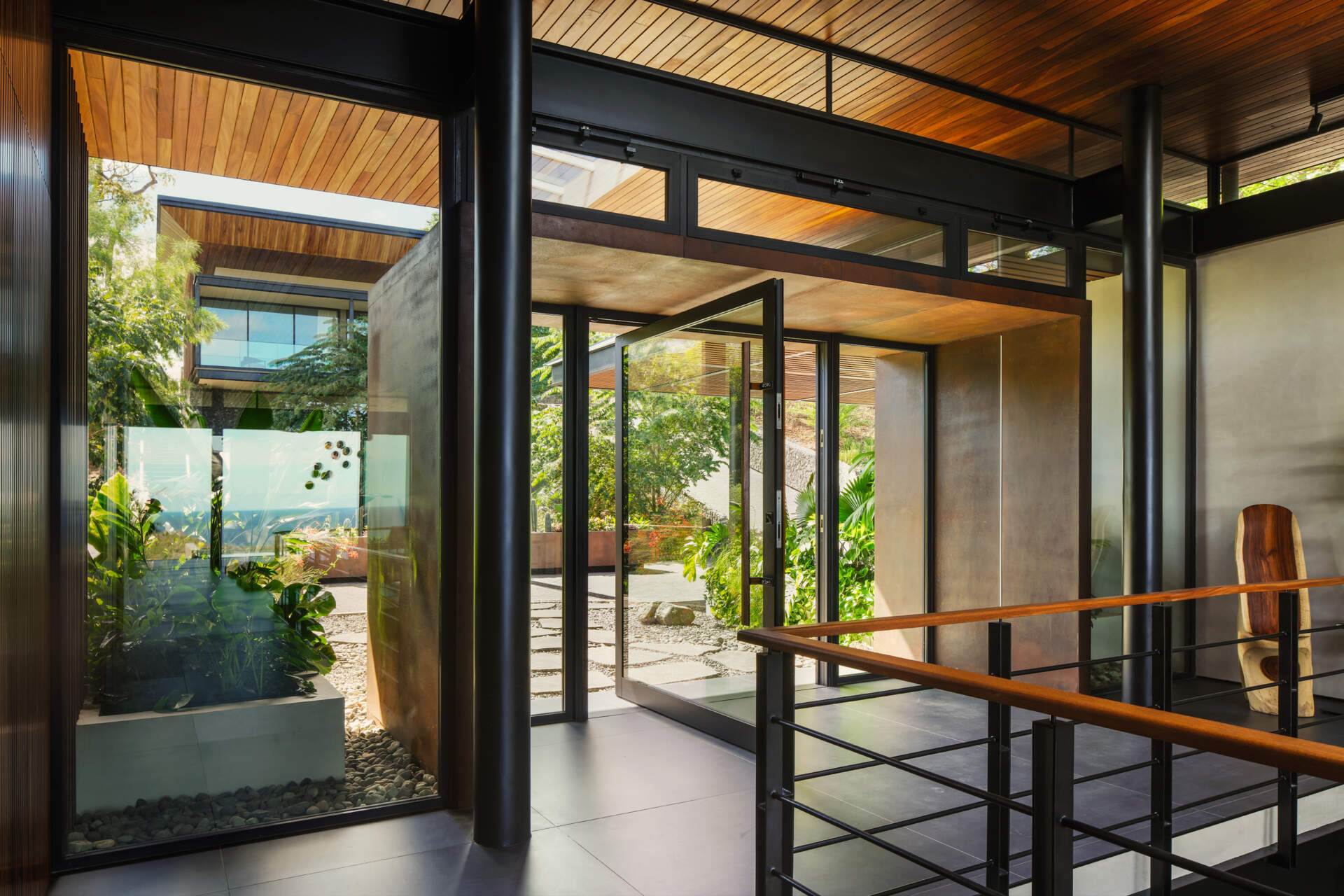 Stone pathways, warm timber, and tropical planting create an entrance that gradually introduces visitors to Casa Akíga.