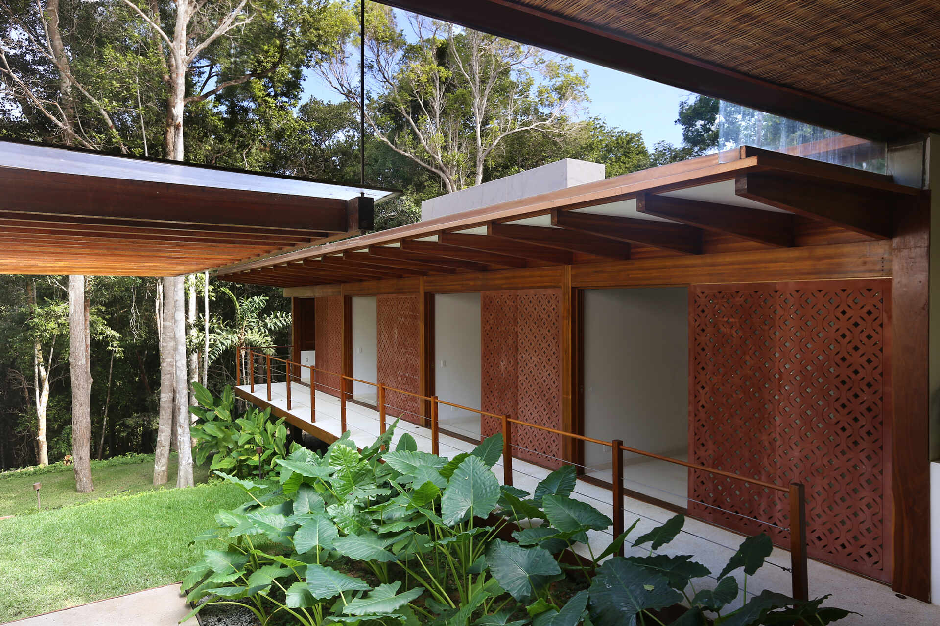 A shaded walkway lined with geometric screens connects the guest suites while overlooking lush gardens and native Atlantic Forest.