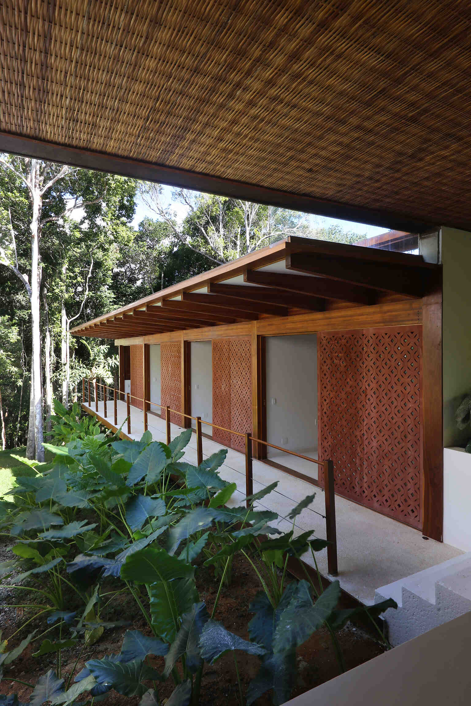 A shaded walkway lined with geometric screens connects the guest suites while overlooking lush gardens and native Atlantic Forest.