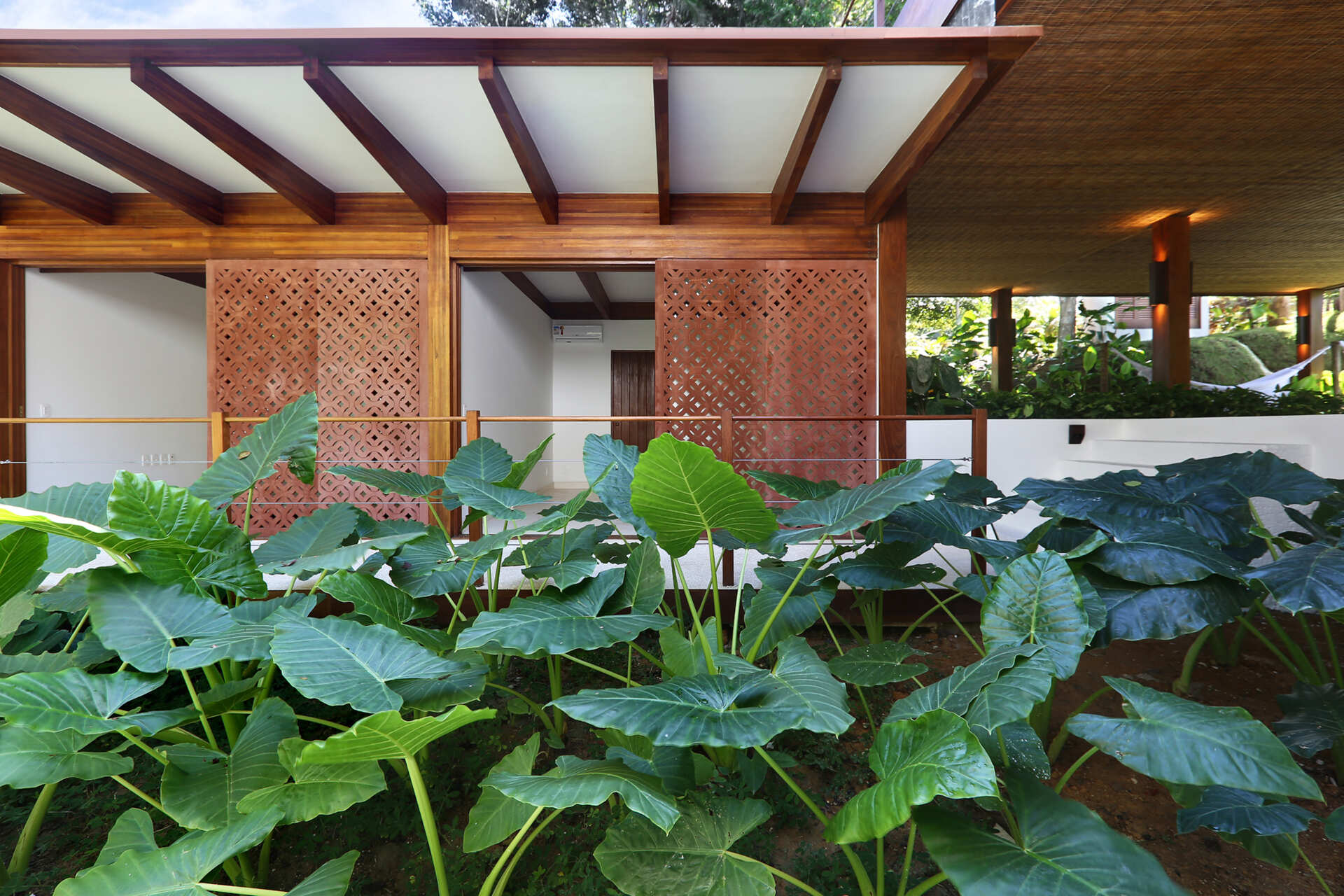 A shaded walkway lined with geometric screens connects the guest suites while overlooking lush gardens and native Atlantic Forest.
