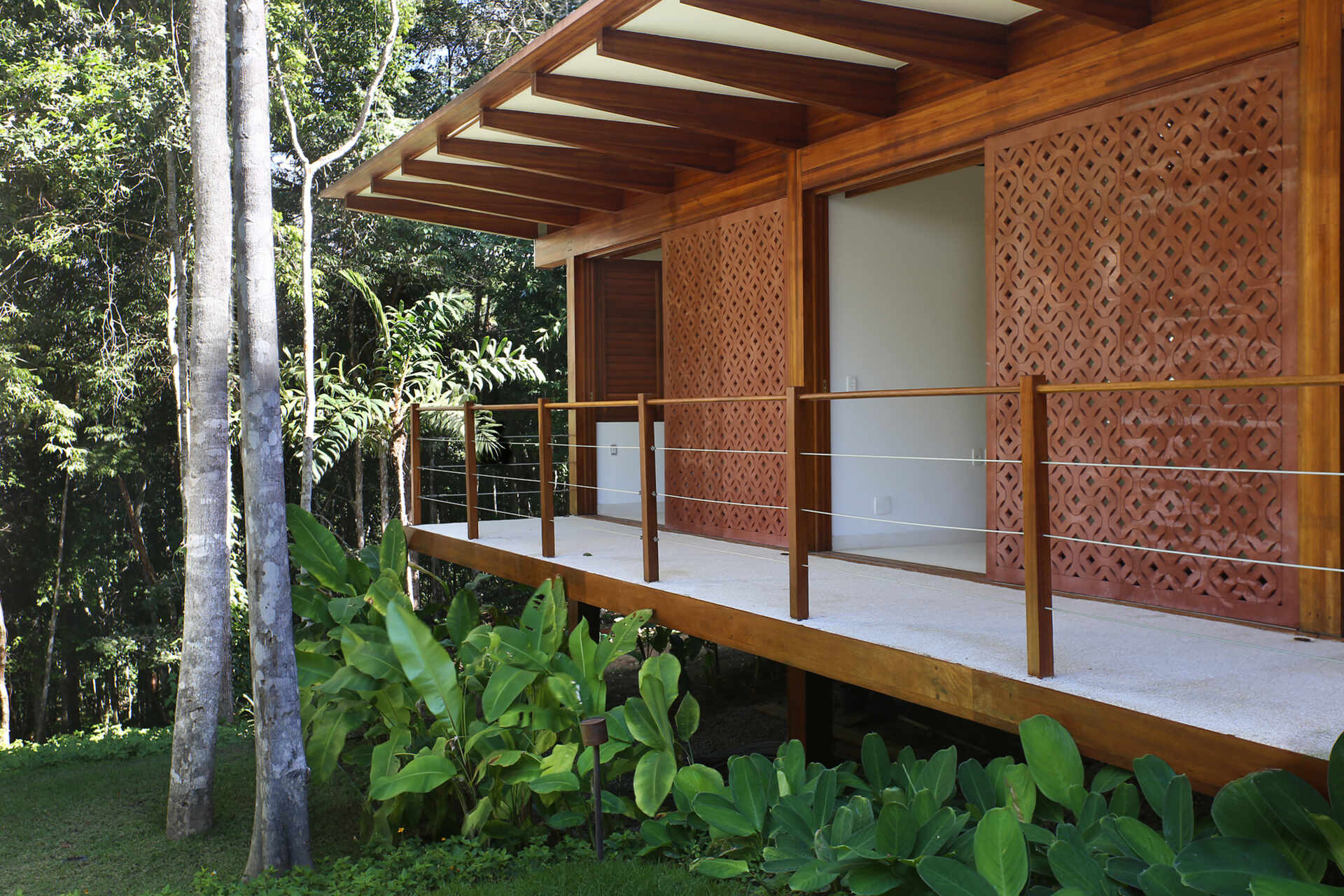 A shaded walkway lined with geometric screens connects the guest suites while overlooking lush gardens and native Atlantic Forest.