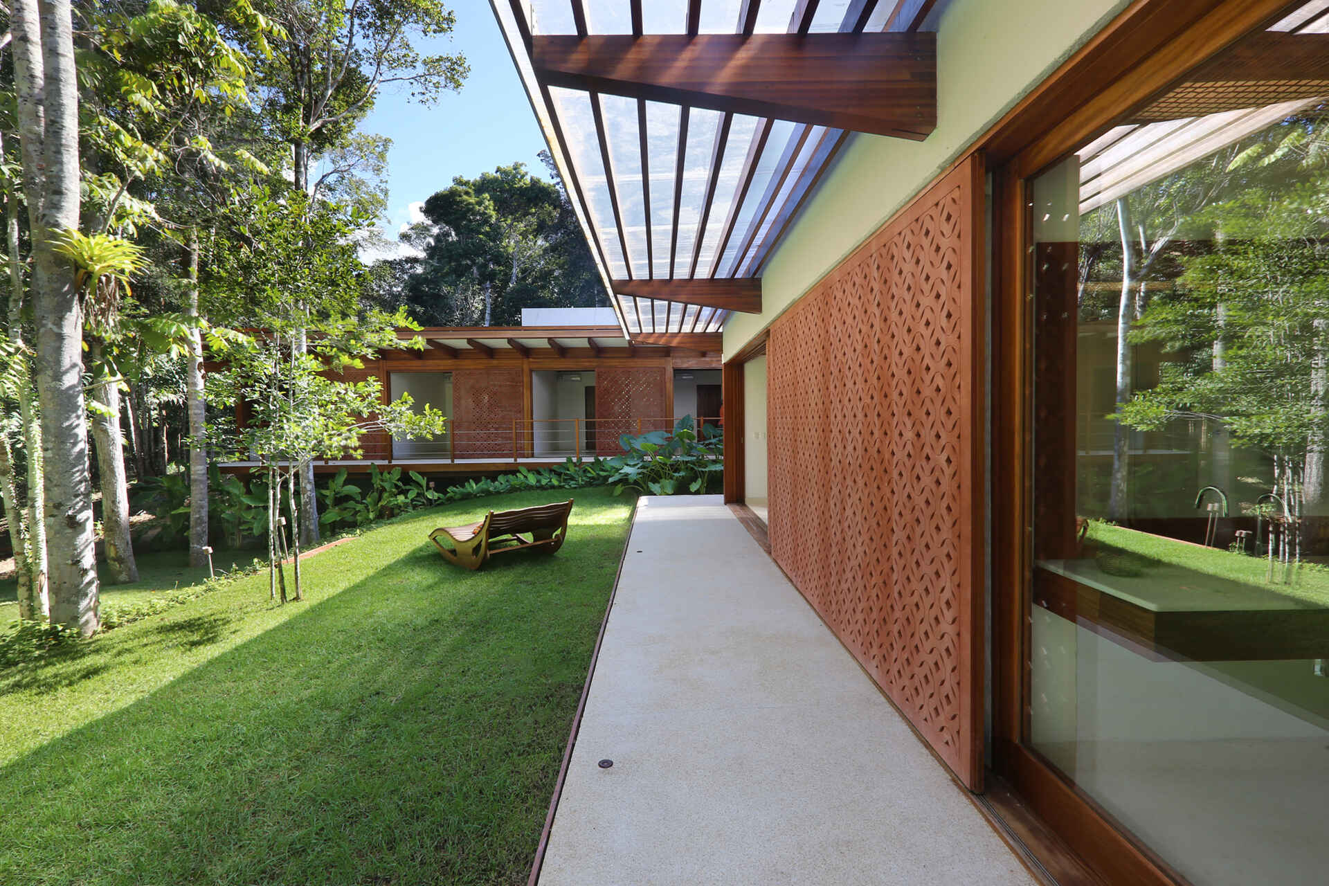 A shaded walkway lined with geometric screens connects the guest suites while overlooking lush gardens and native Atlantic Forest.