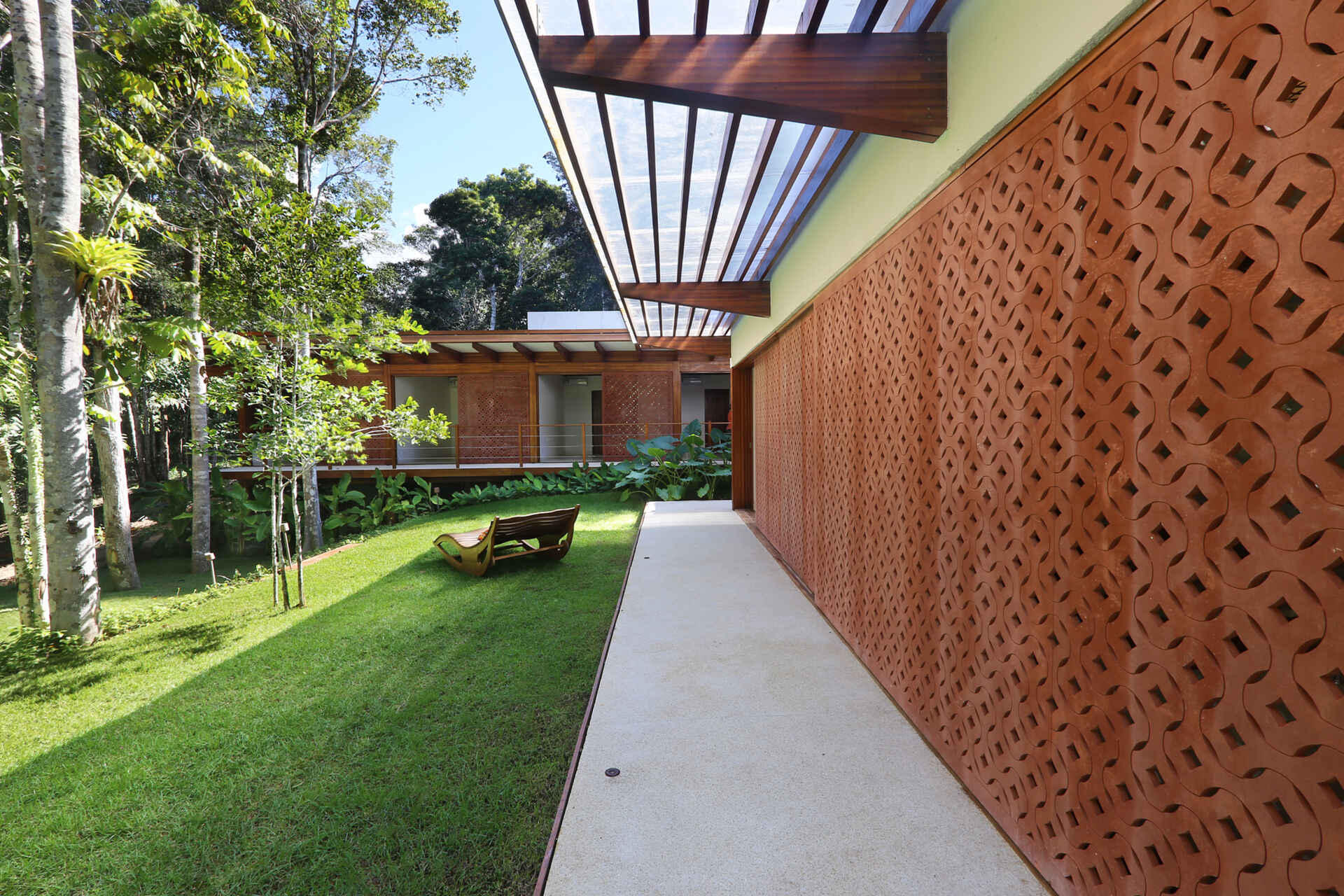 A shaded walkway lined with geometric screens connects the guest suites while overlooking lush gardens and native Atlantic Forest.
