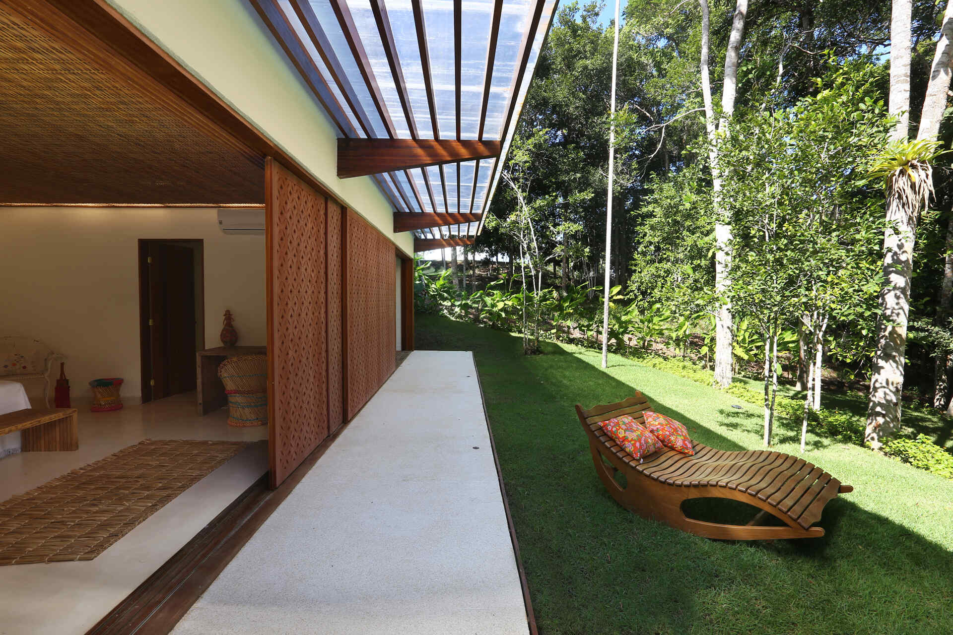 A shaded walkway lined with geometric screens connects the guest suites while overlooking lush gardens and native Atlantic Forest.