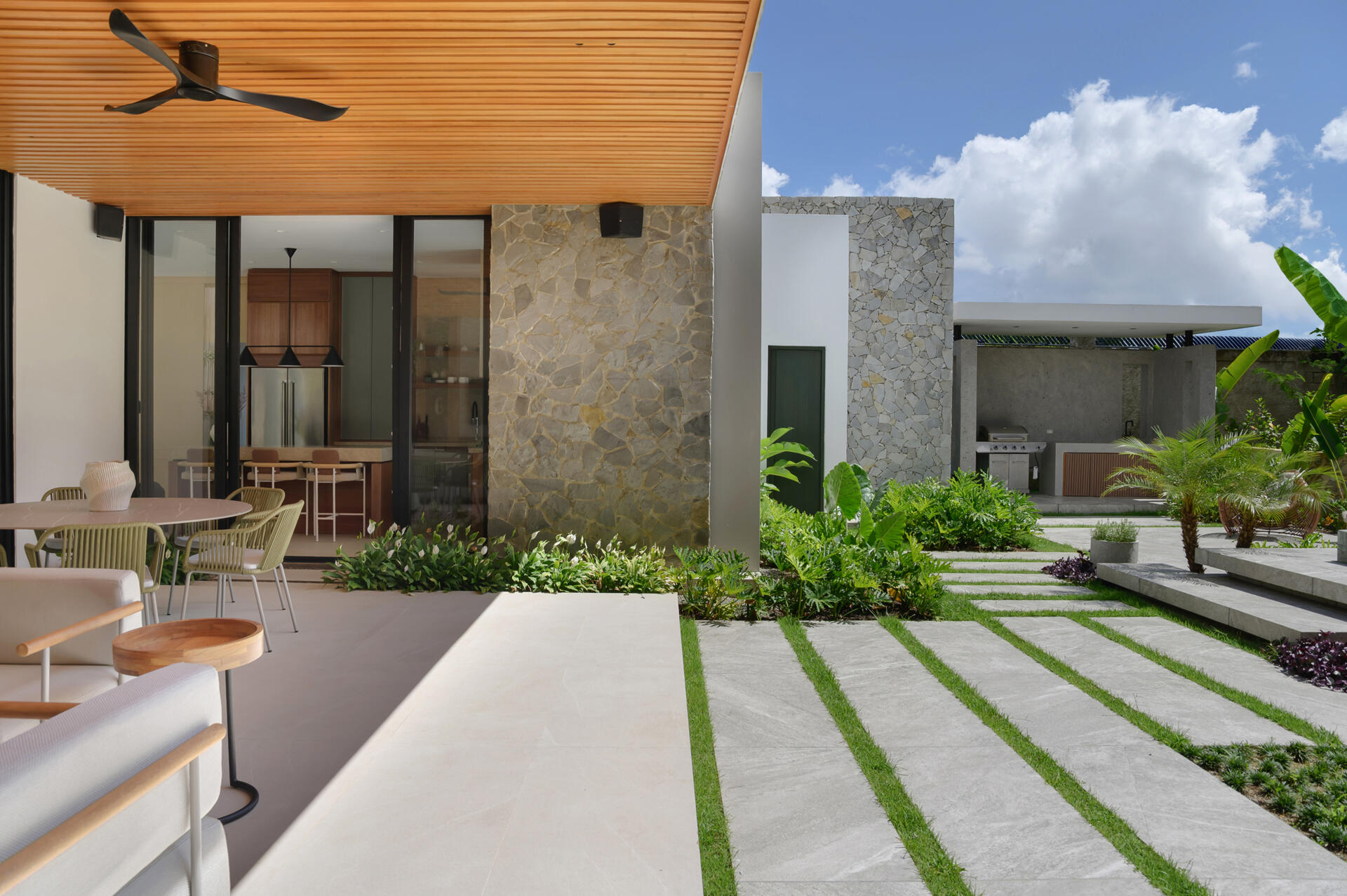 Step onto a modern patio featuring a timber-lined ceiling, lush tropical landscaping, stone pathways and seamless indoor-outdoor living.