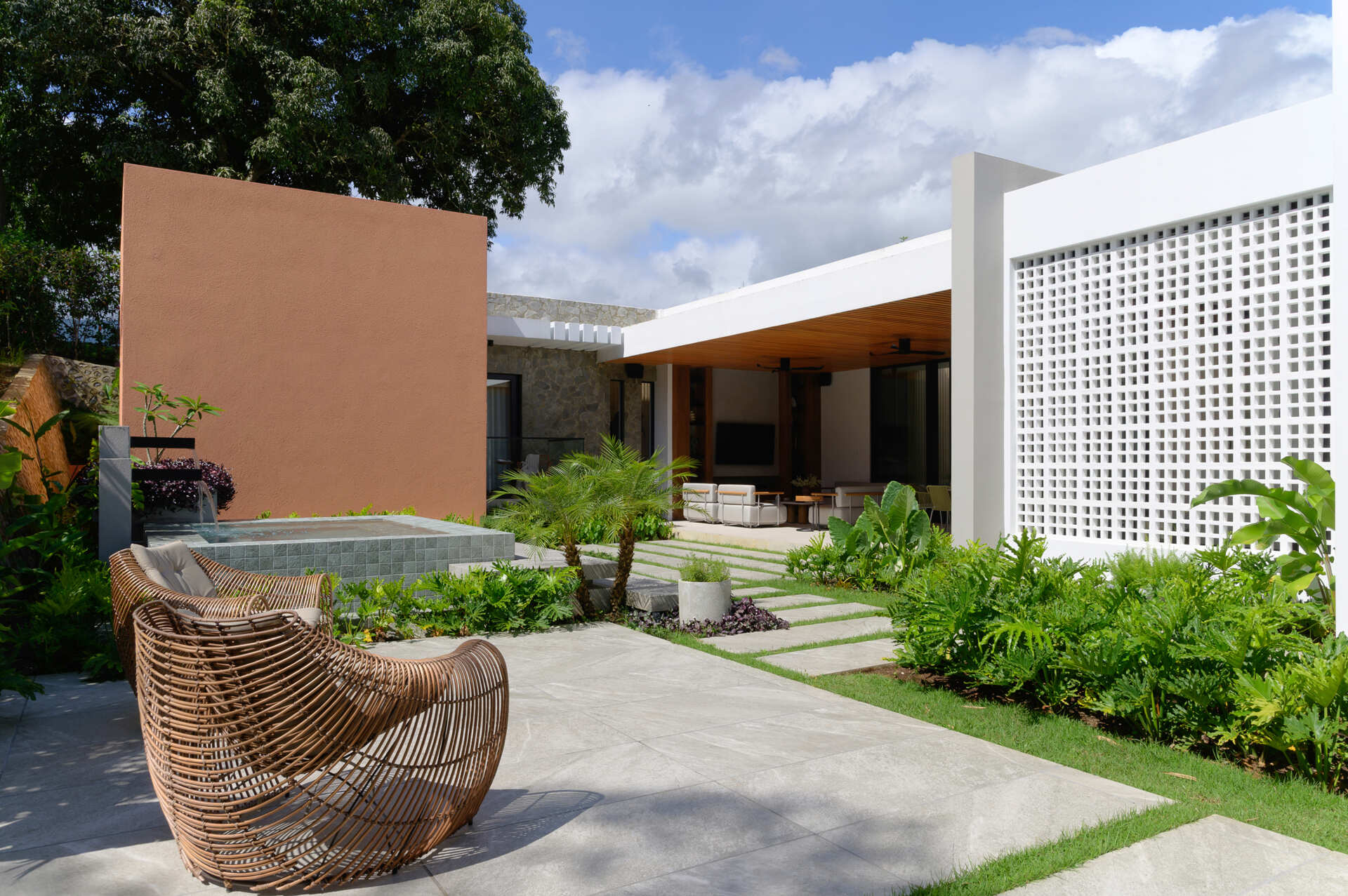 Step onto a modern patio featuring a timber-lined ceiling, lush tropical landscaping, stone pathways and seamless indoor-outdoor living.