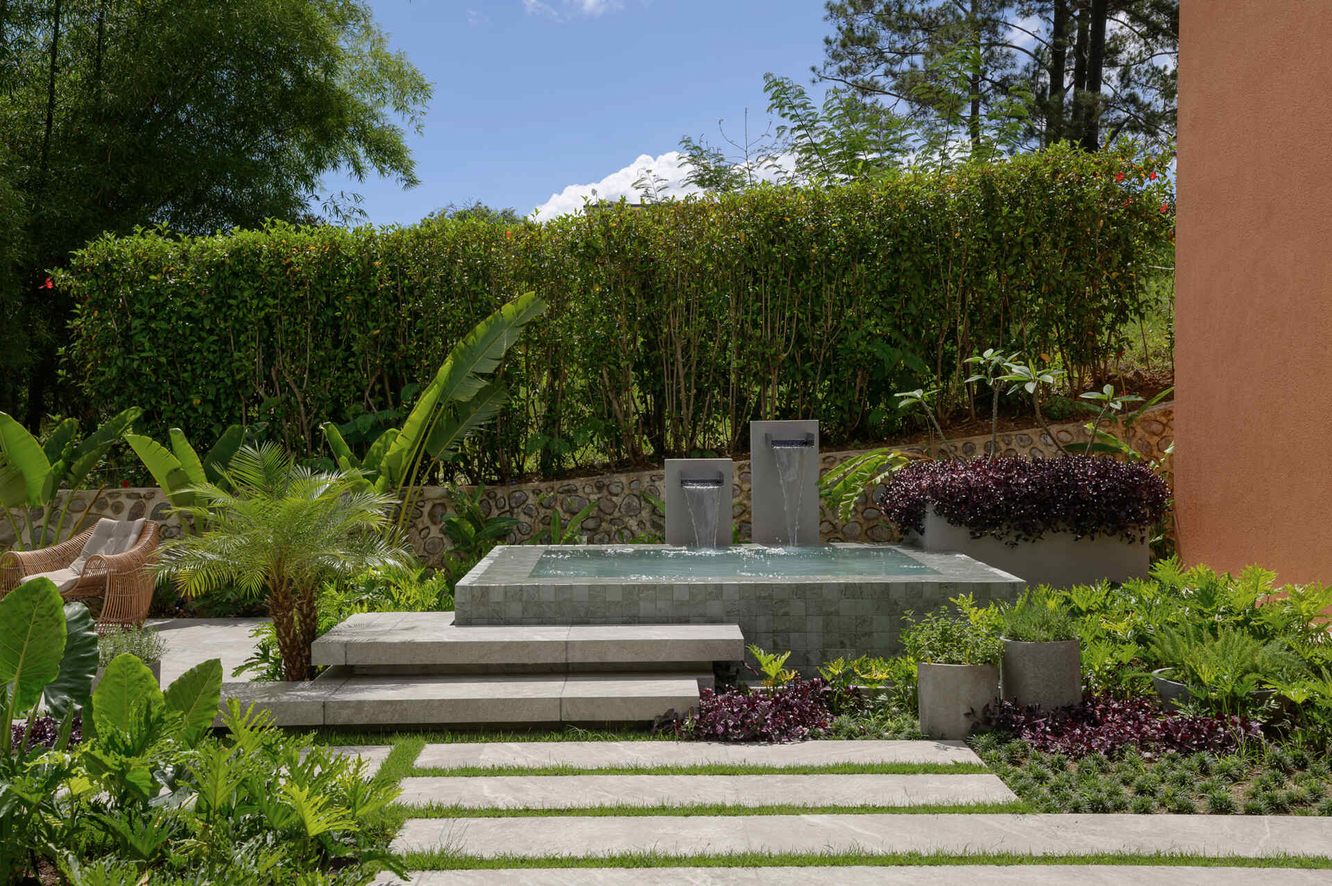 Step onto a modern patio featuring a timber-lined ceiling, lush tropical landscaping, stone pathways and seamless indoor-outdoor living.