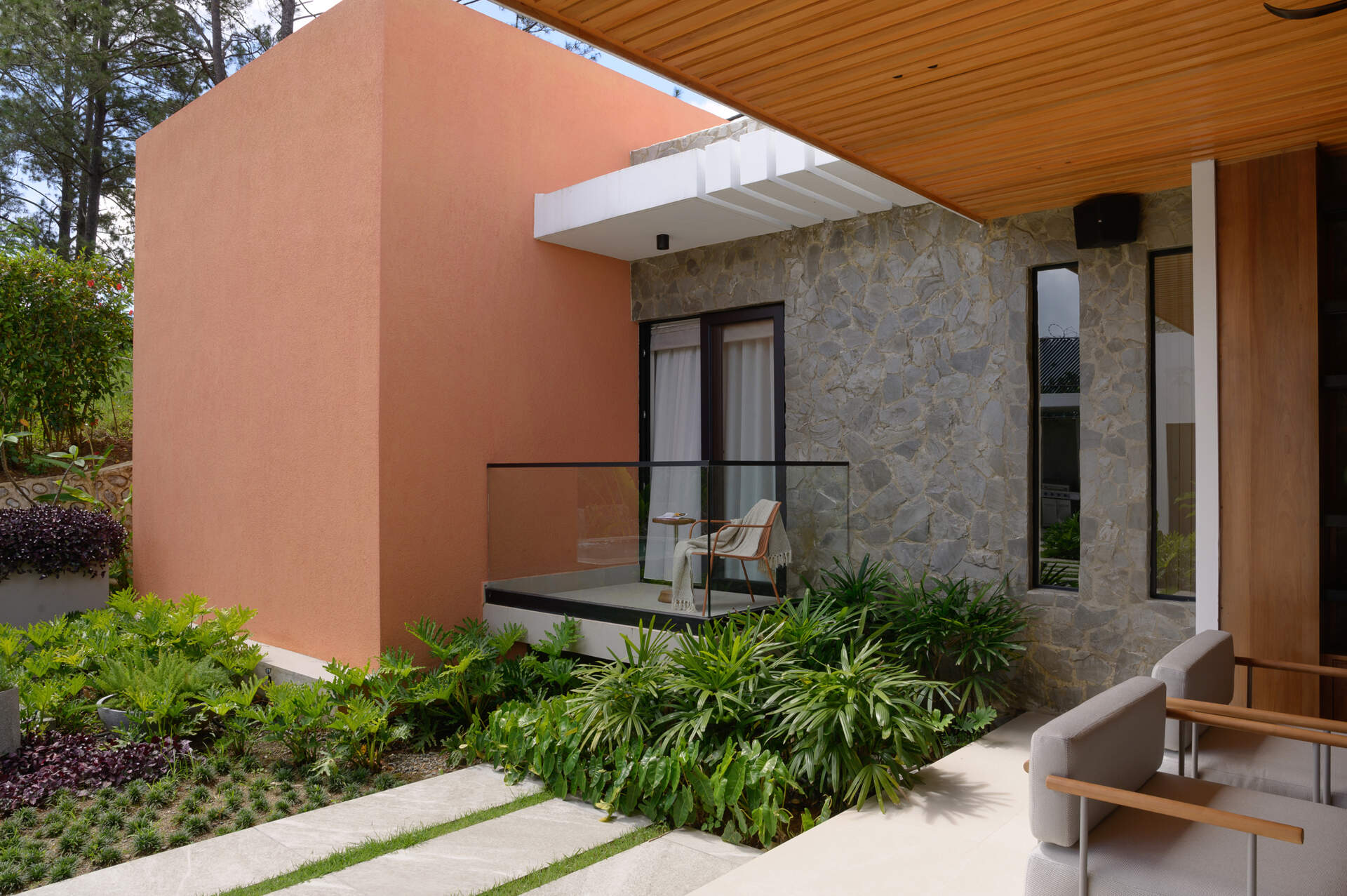 Step onto a modern patio featuring a timber-lined ceiling, lush tropical landscaping, stone pathways and seamless indoor-outdoor living.