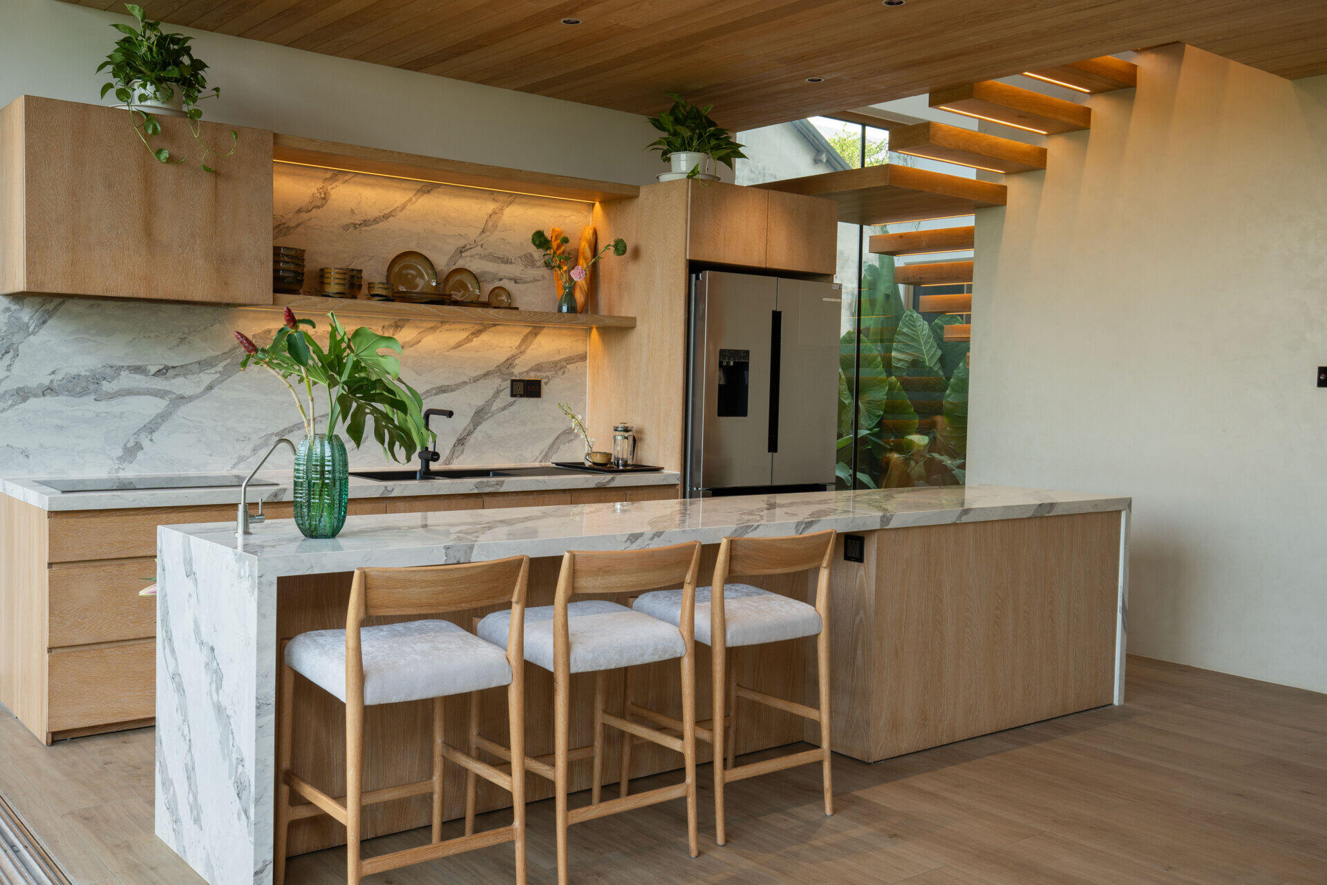 This warm, open kitchen pairs timber cabinetry, marble surfaces and a generous island with garden views, creating a bright space that flows naturally into the surrounding tropical landscape.