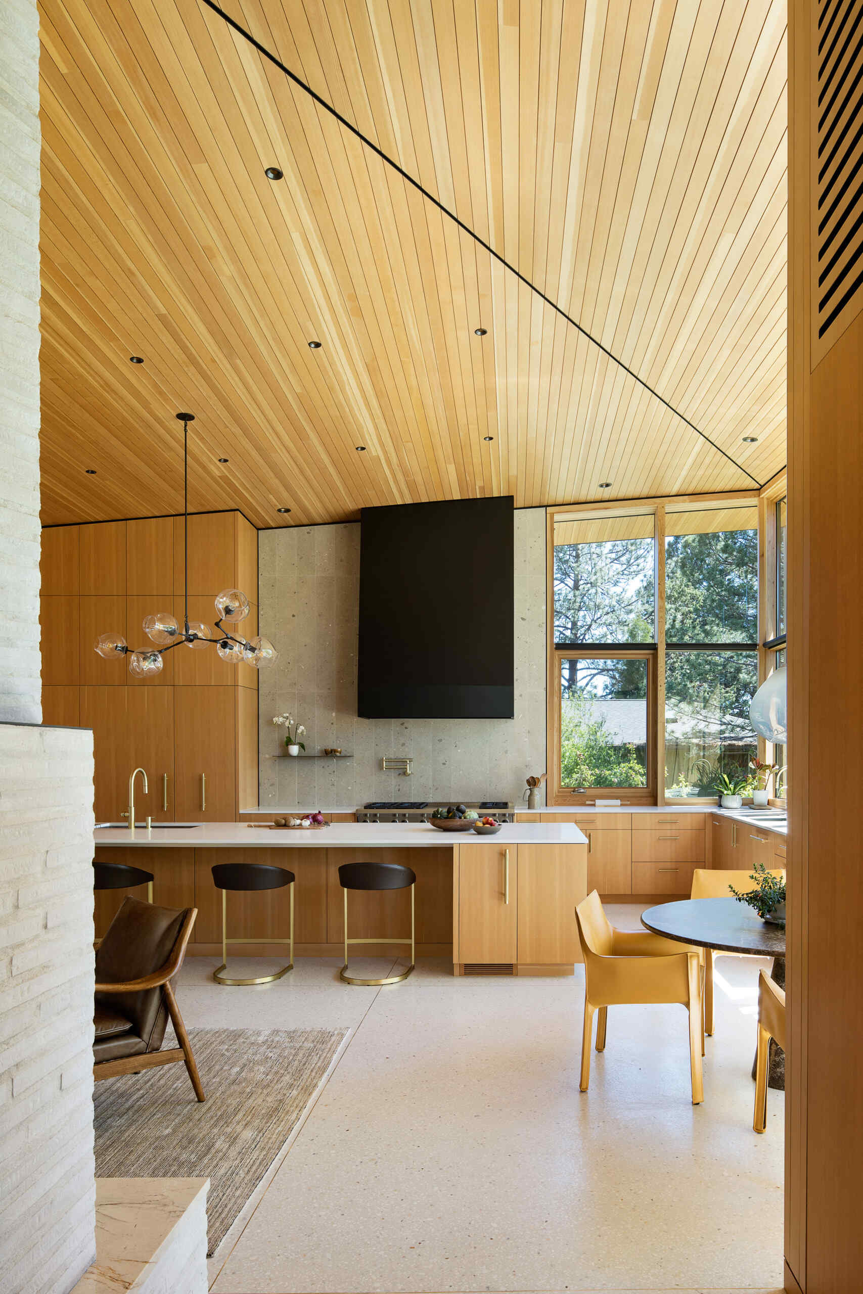 Visite la cocina moderna y luminosa con cálidos gabinetes de madera, una isla blanca y un tranquilo rincón para desayunar con vista a los árboles circundantes.