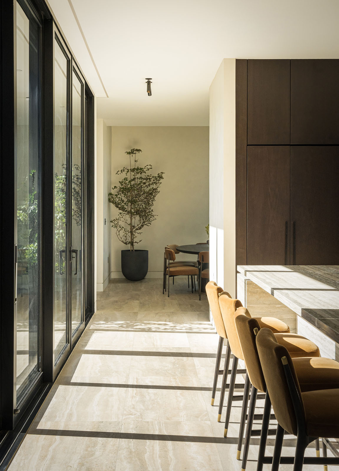 This light-filled dining room combines soaring corner glazing, warm timber cabinetry, and a round dining table to create an elegant space for everyday meals and entertaining.