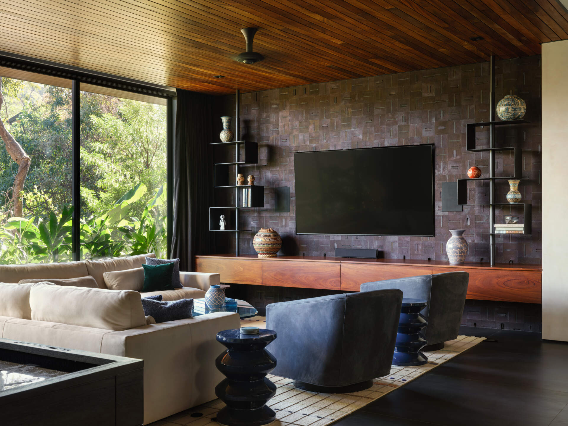 This media and games room at Casa Akíga combines warm timber finishes, custom cabinetry, colourful artwork, and jungle views to create a relaxed entertainment space with plenty of personality.