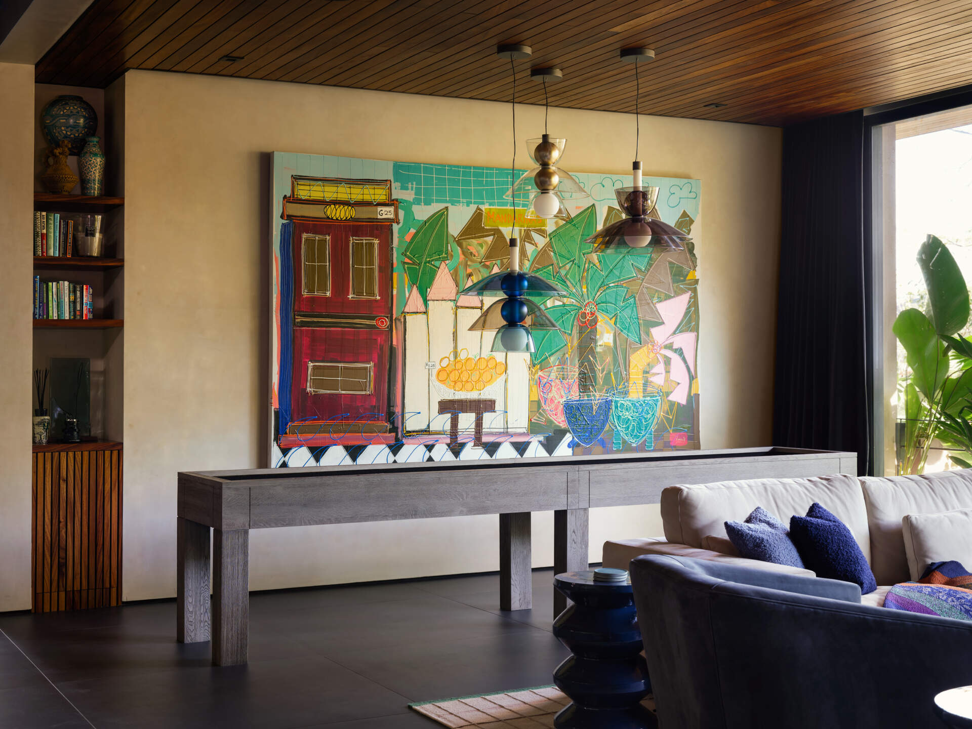 This media and games room at Casa Akíga combines warm timber finishes, custom cabinetry, colourful artwork, and jungle views to create a relaxed entertainment space with plenty of personality.
