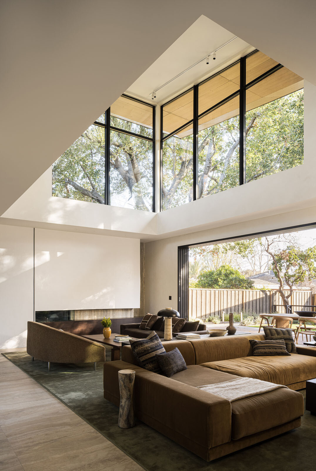 Step inside a bright double-height living room where floor-to-ceiling glazing frames a mature redwood tree, filling this modern Silicon Valley home with natural light and garden views.