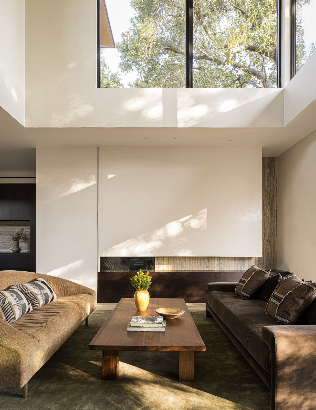 Step inside a bright double-height living room where floor-to-ceiling glazing frames a mature redwood tree, filling this modern Silicon Valley home with natural light and garden views.