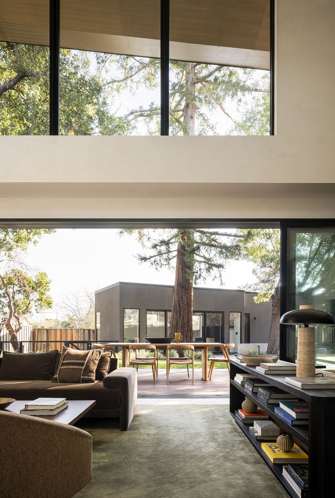 Step inside a bright double-height living room where floor-to-ceiling glazing frames a mature redwood tree, filling this modern Silicon Valley home with natural light and garden views.