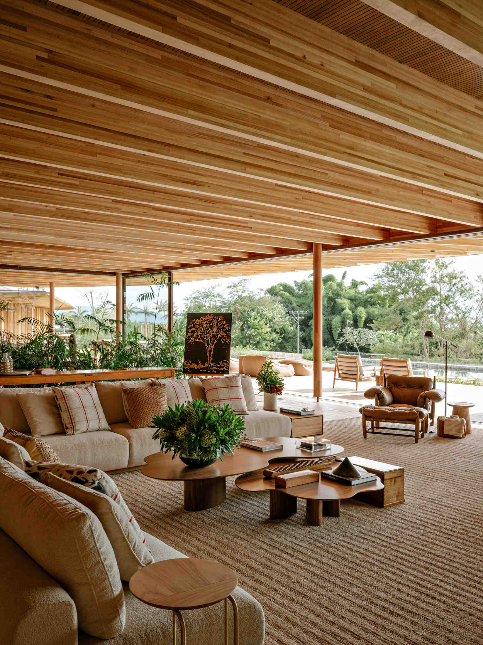 Visite una sala de estar con altísimas vigas de madera, pisos de travertino, iluminación de cobre y una pared de vidrio con vista al bosque.