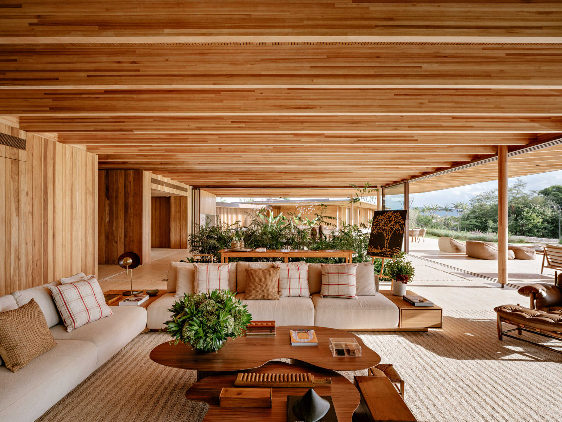 Visite una sala de estar con altísimas vigas de madera, pisos de travertino, iluminación de cobre y una pared de vidrio con vista al bosque.