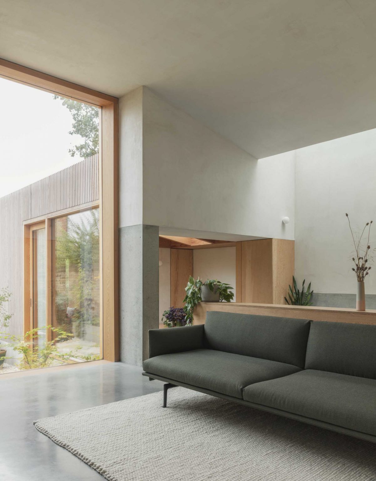 An impressive 11-foot-tall window floods this living room with natural light while framing views of the sheltered courtyard and showcasing the timber extension.