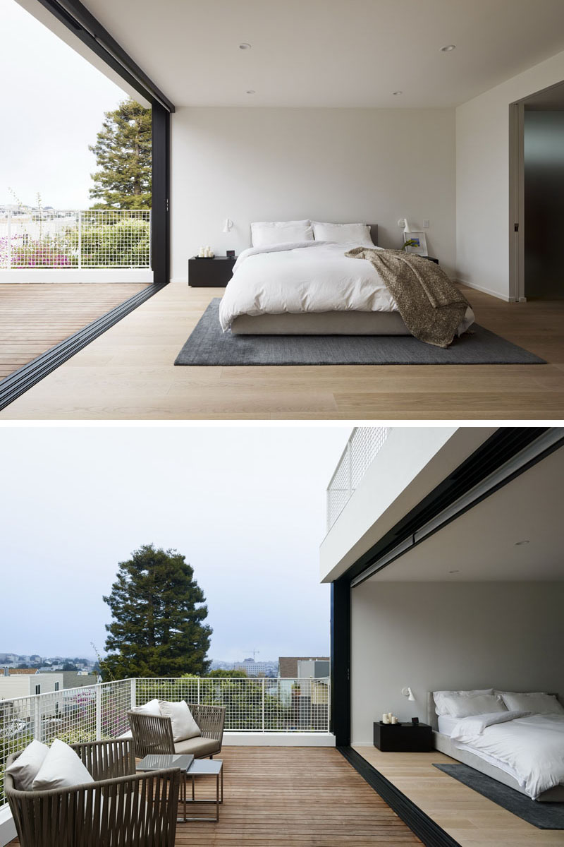 This modern bedroom and bathroom pair features a private balcony and a timber wall behind the freestanding bathtub.