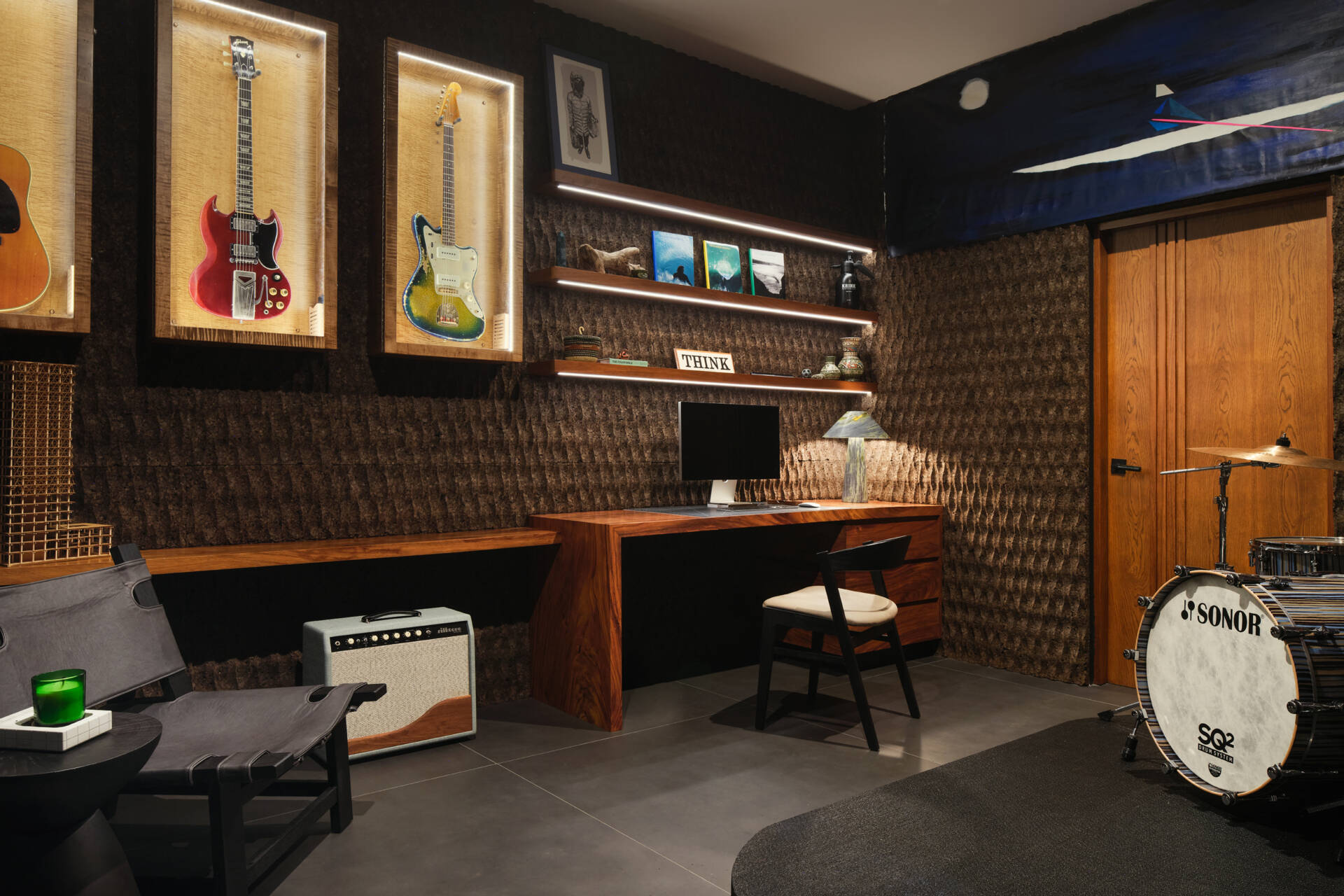 Part office, part music studio, this creative room at Casa Akíga combines custom timber joinery, illuminated guitar displays, textured walls, and warm lighting into a space designed for work and inspiration.