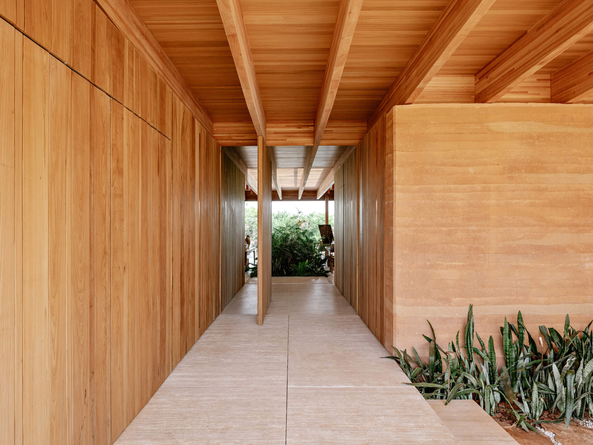 Descubra cómo las llamativas puertas pivotantes de madera crean una transición perfecta de un exterior texturizado a un interior cálido y contemporáneo.
