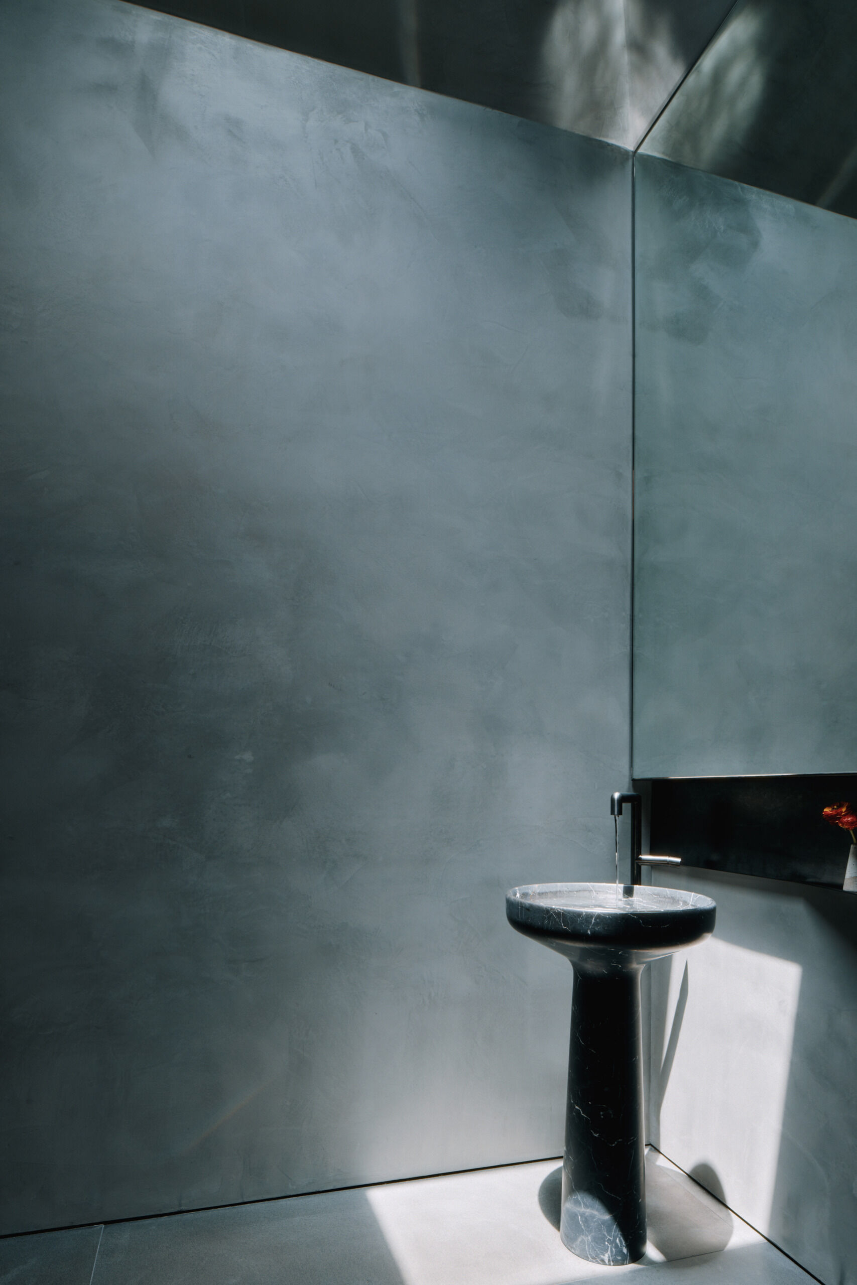 Although compact, the powder room offers a more minimalist approach with darker surfaces, a large mirror, and a sculptural pedestal sink.