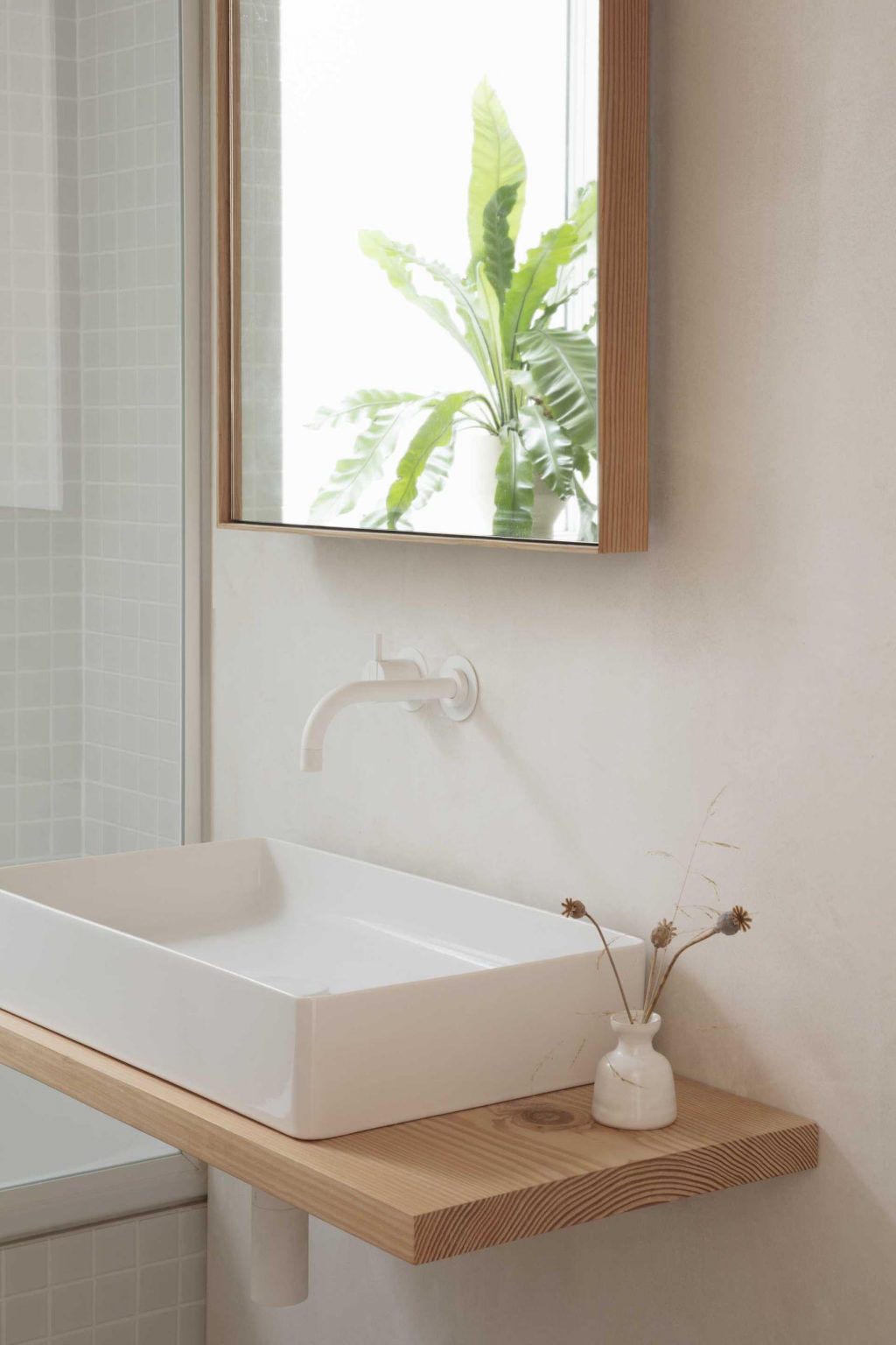 Small square tiles wrap the bath and shower area while timber accents around the mirror and vanity bring warmth to this compact contemporary bathroom.