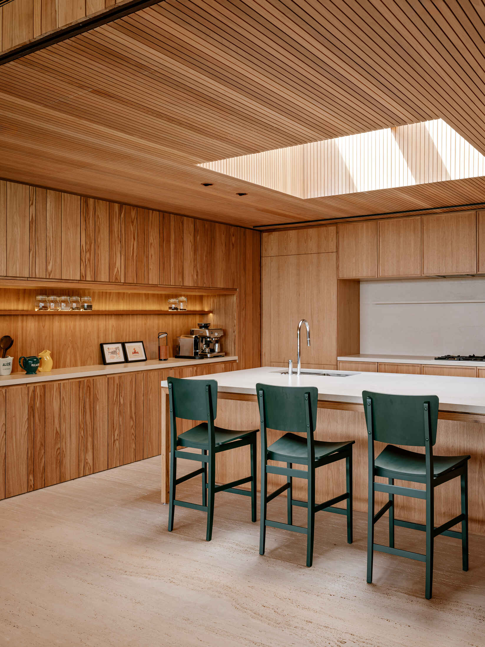 Descubra una cálida cocina de madera con tragaluces, gabinetes integrados, una gran isla blanca y taburetes verdes que agregan sutiles toques de color.
