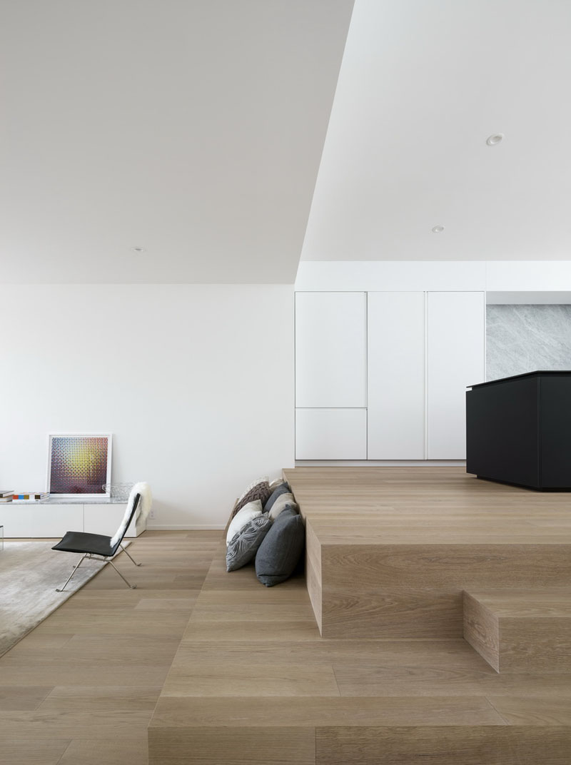 Explore a minimalist kitchen with a bold black island, hidden powder room, timber seating steps, and clever modern details.