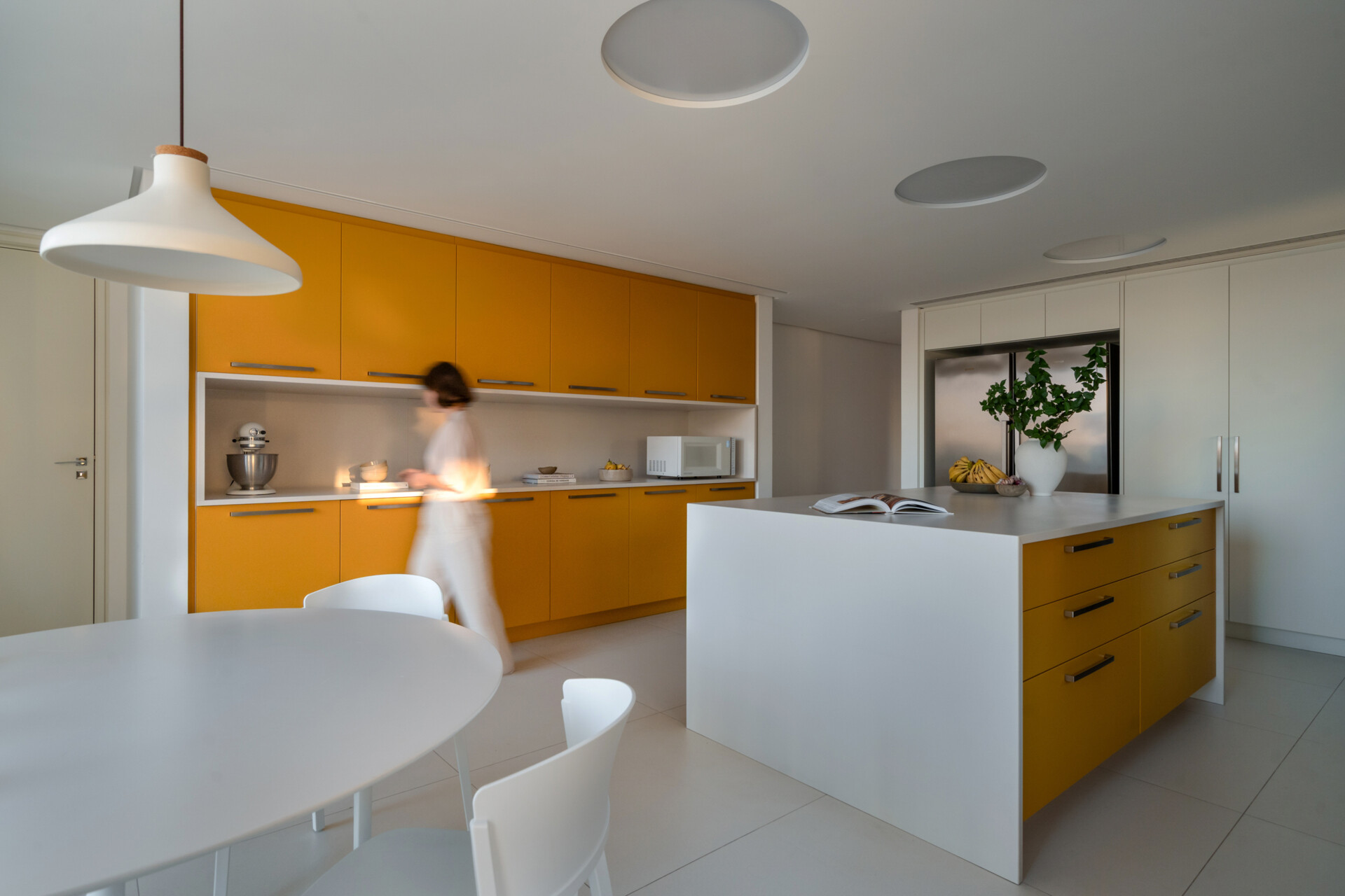 Behind warm timber panels is a cheerful kitchen where pale cabinetry meets bold mustard-yellow storage.